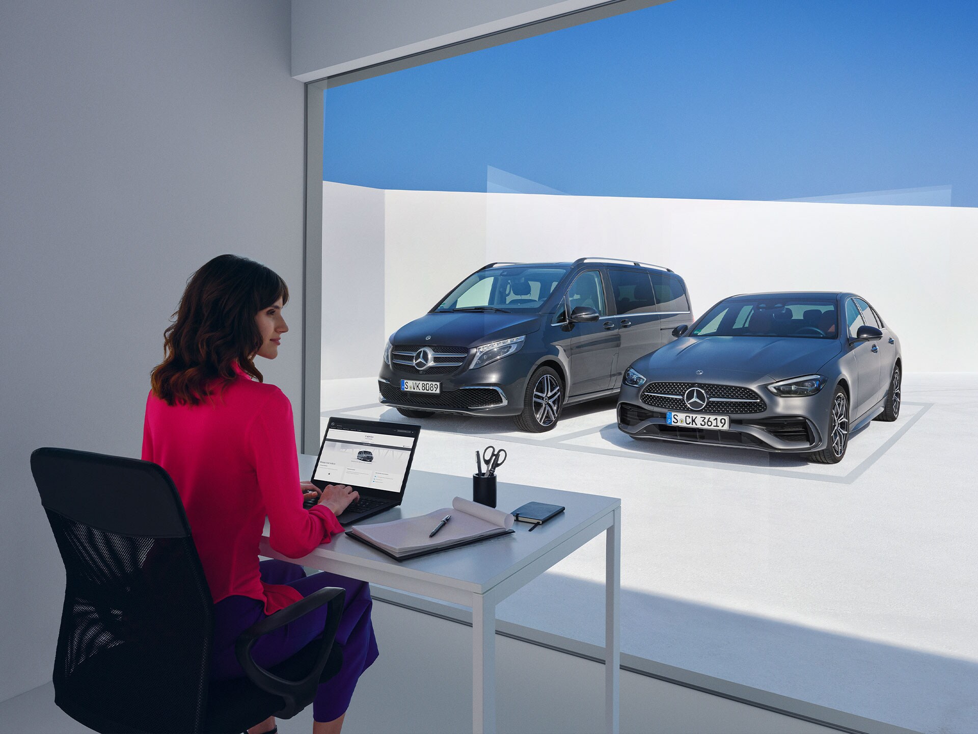 Women sitting in front of the Mercedes-Benz V-Class and C-Class and looking at a laptop.
