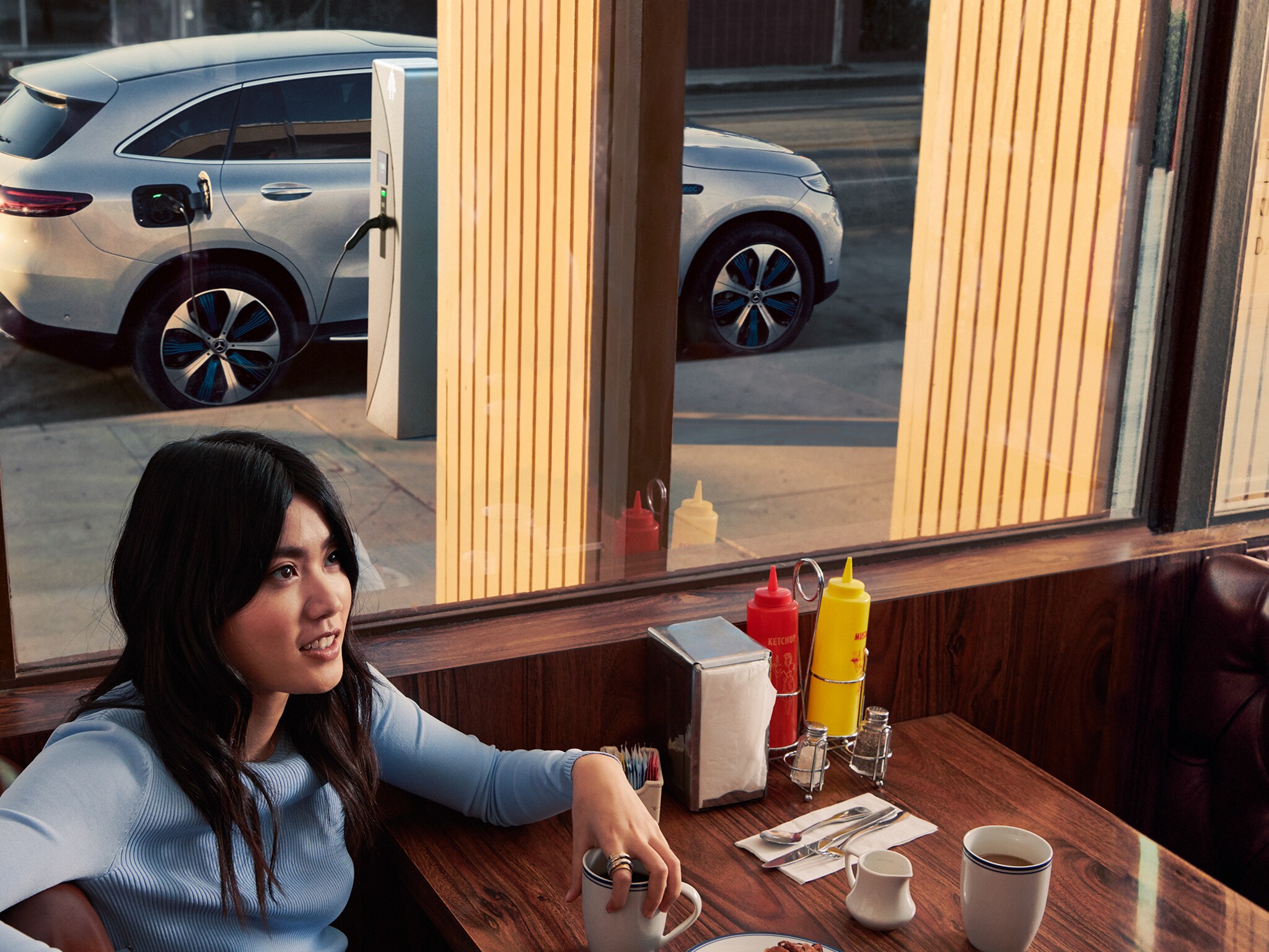 Woman in diner with charging Mercedes-Benz seen outside window