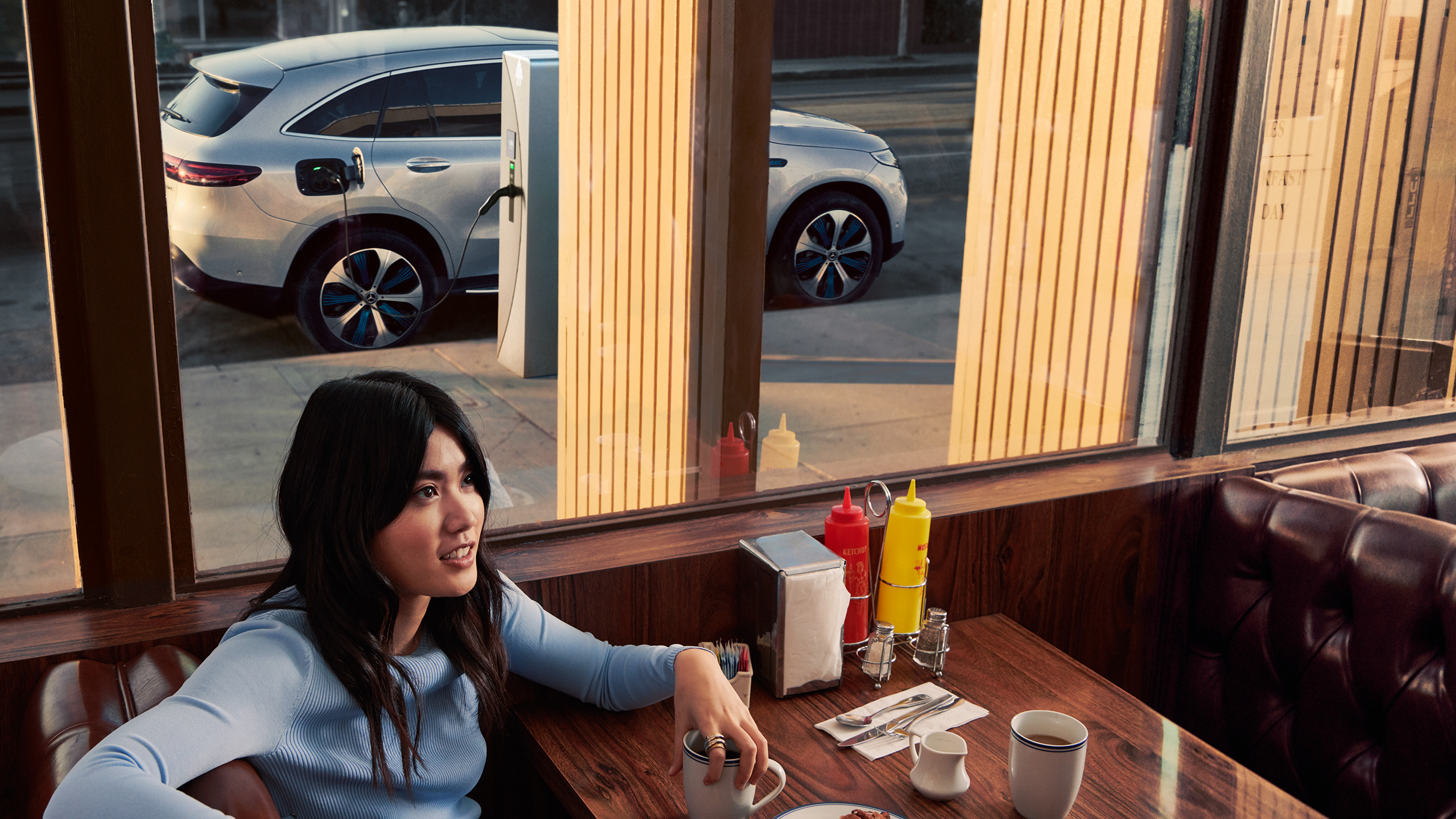 Mercedes-Benz Public Charging Woman in diner with charging Mercedes-Benz seen outside window