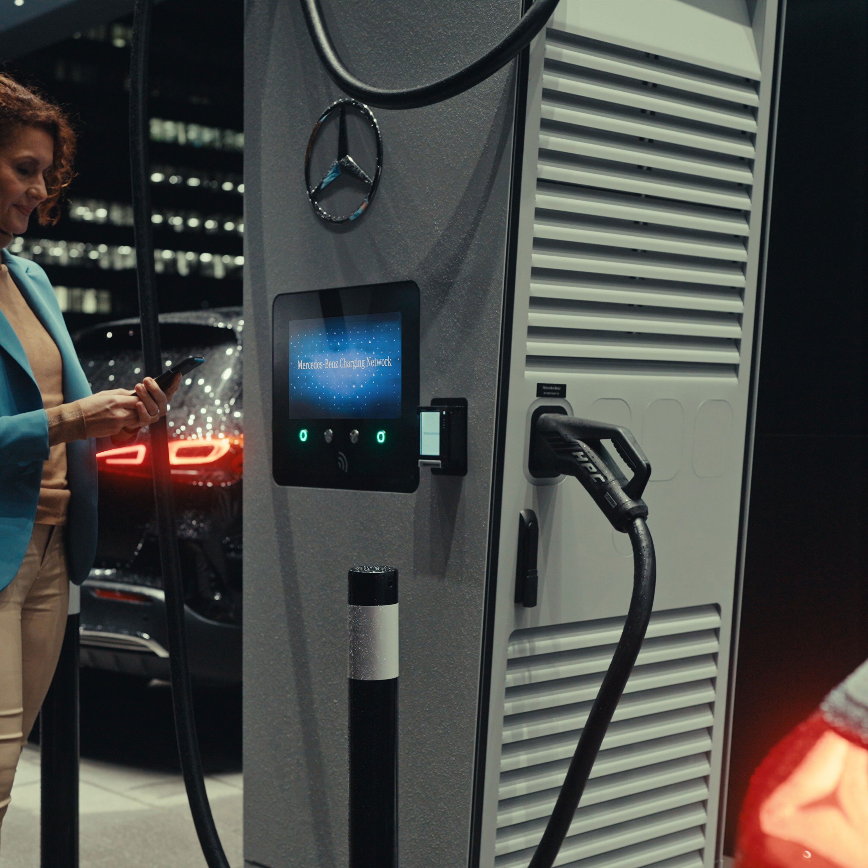 A woman holding a smartphone in her hand, standing next to a charging station.
