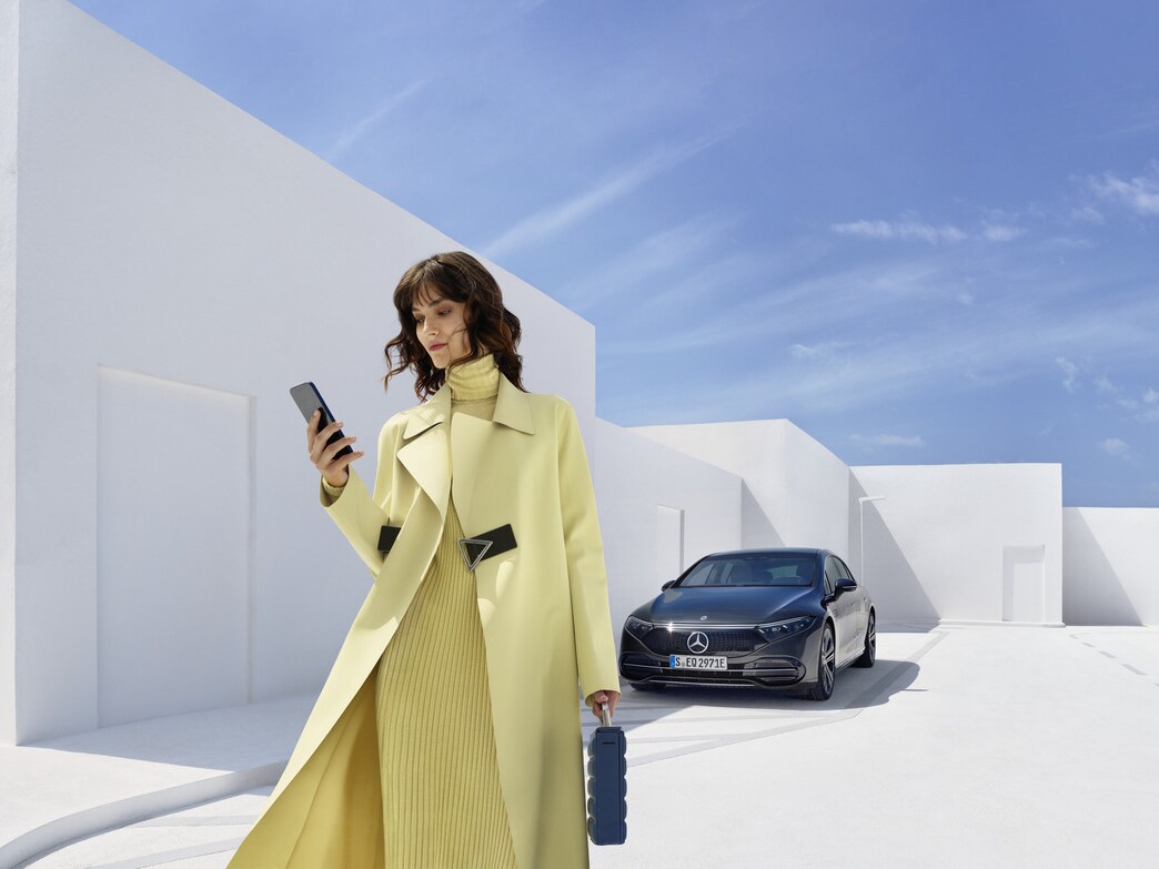 A woman with her smartphone is standing in front of a Mercedes-Benz.