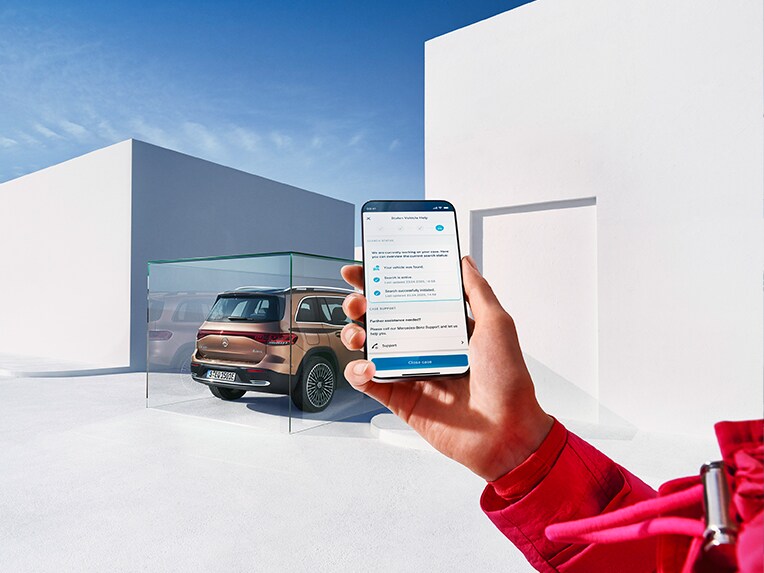 Someone holding a cell phone in the cell phone and using the Mercedes me App. An EQB is parked in the background.