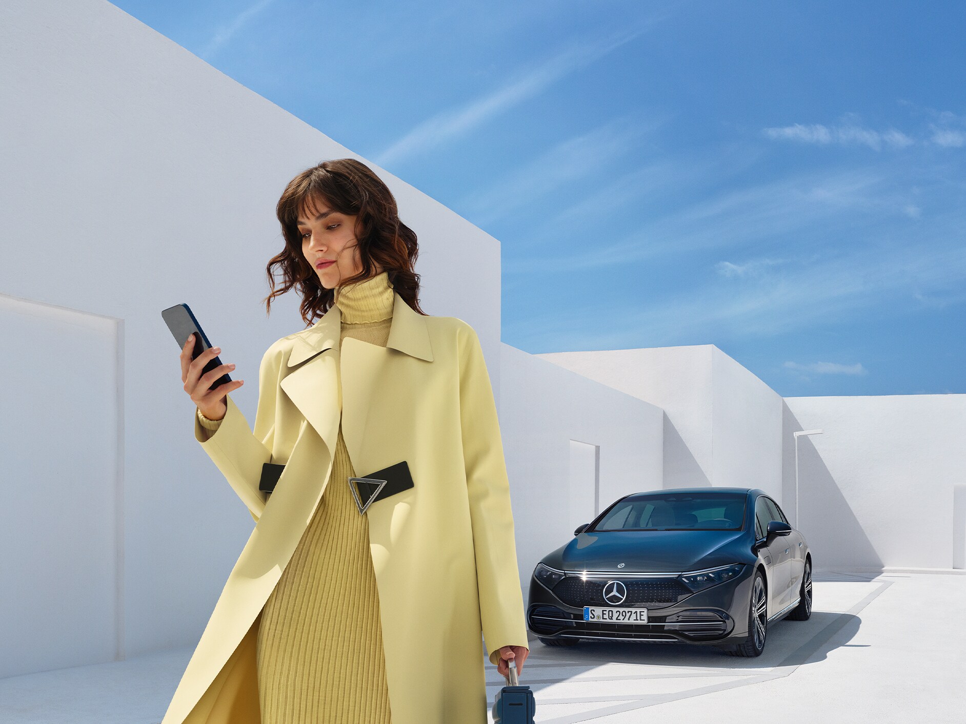 Woman looking at her cell phone as she walks away from her Mercedes-EQ vehicle.