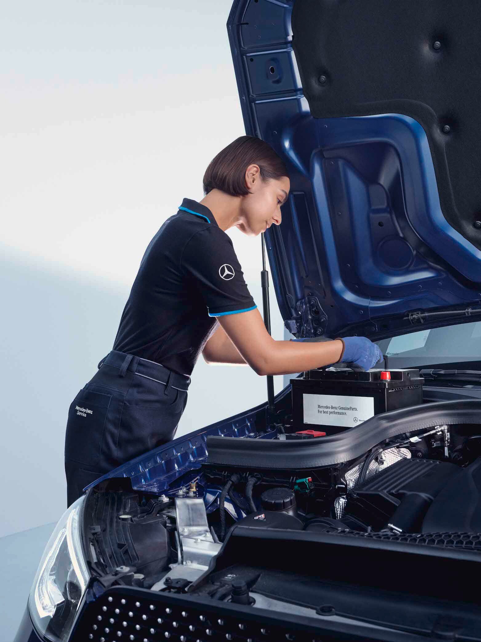 A automotive mechanic bends over the open bonnet of a Mercedes-Benz.