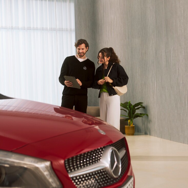 A woman stands in front of a Mercedes-Benz vehicle.
