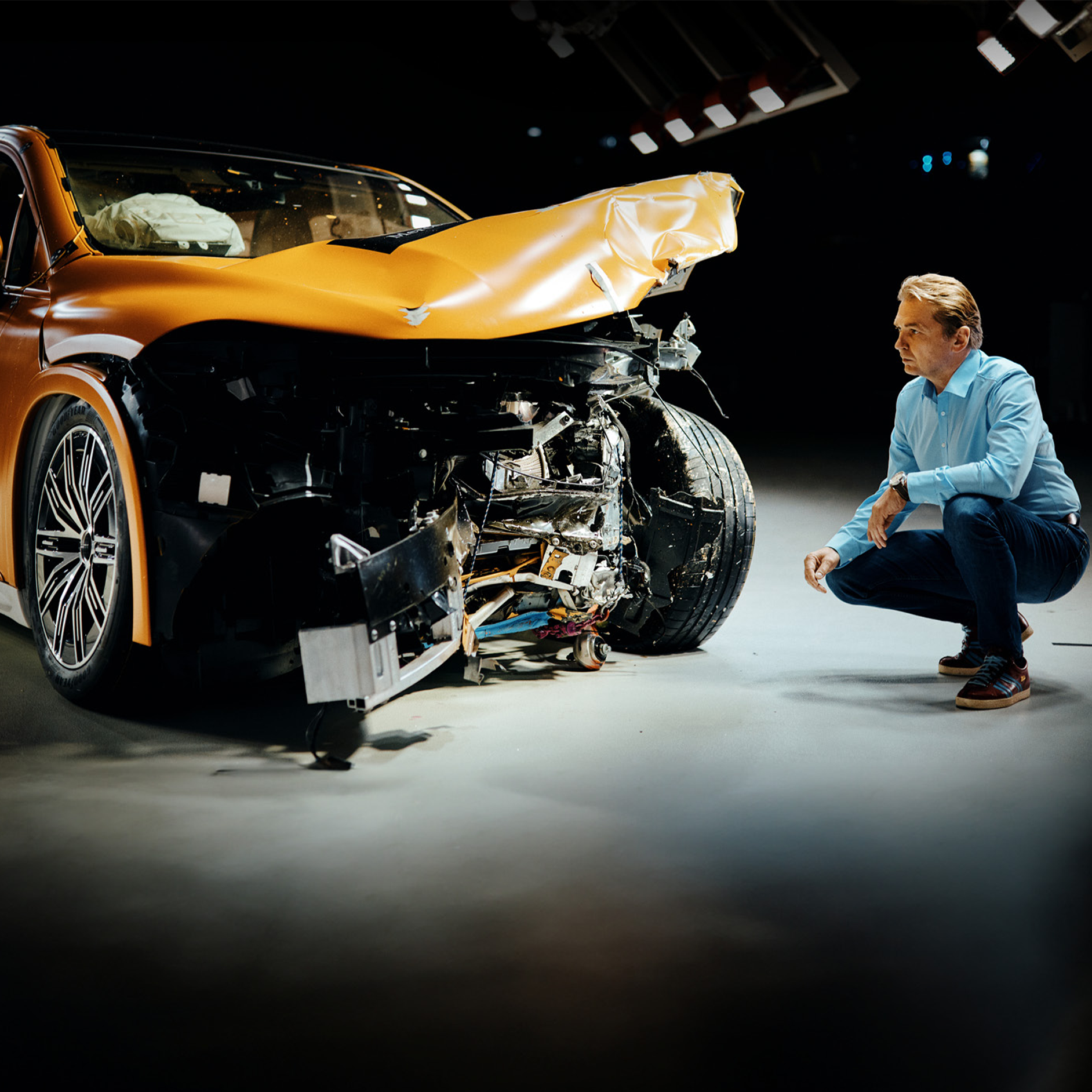 Crash test experts | Safety | Mercedes-Benz Crash test expert examing front-crashed Mercedes-Benz car while crouching bedite it.