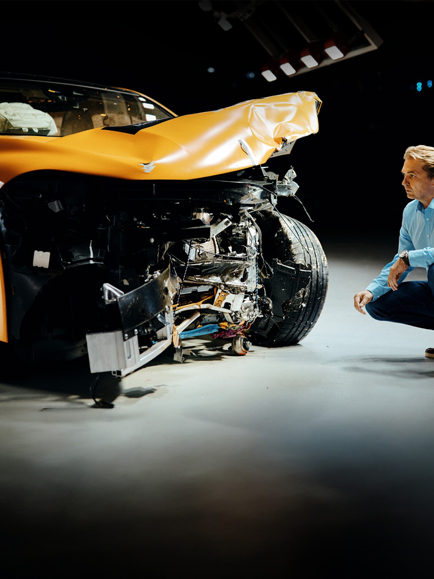 Crash test expert examing front-crashed Mercedes-Benz car while crouching bedite it.