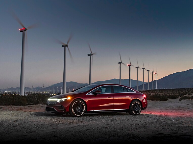 A red Mercedes-Benz EQS (V 297) parked in front of wind turbines.