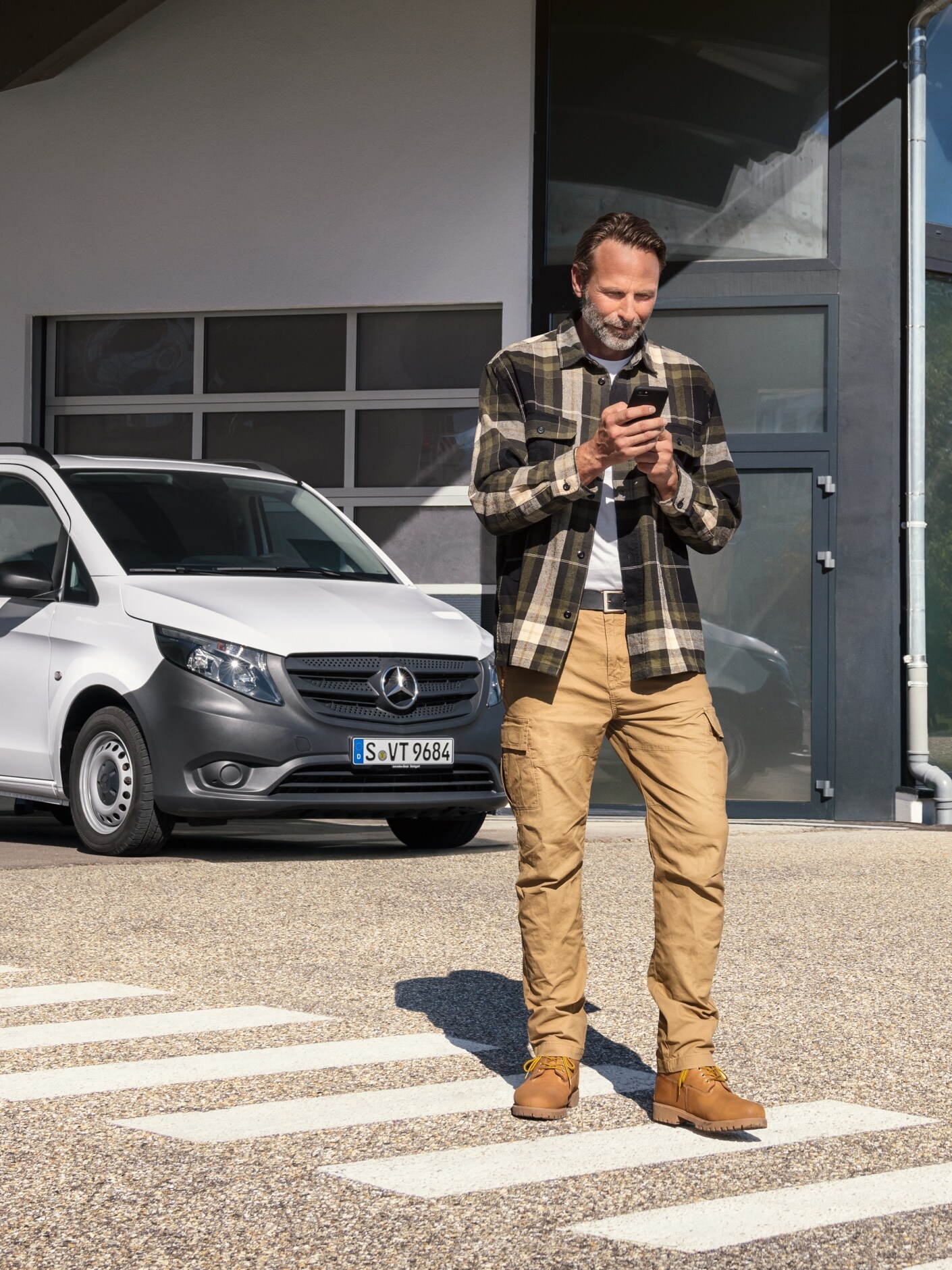 A man standing in front of a white Mercedes-Benz Vito van using his phone. 