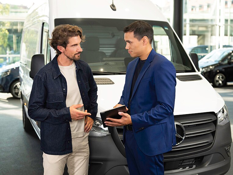 Two people talking and pointing at a mobile device while standing in front of a Mercedes-Benz van.