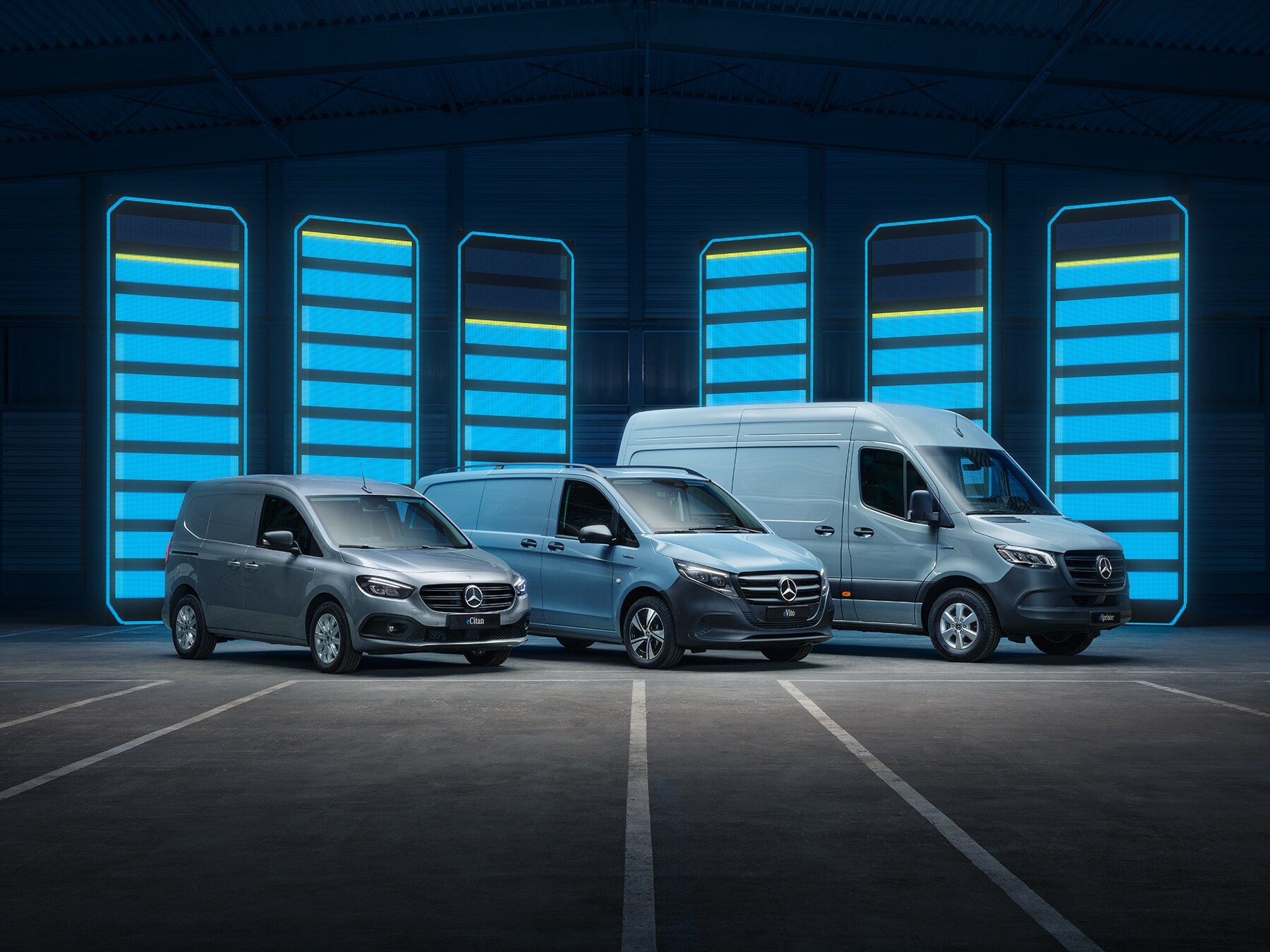 Mercedes-Benz electric van lineup displayed in futuristic warehouse with illuminated charging bars