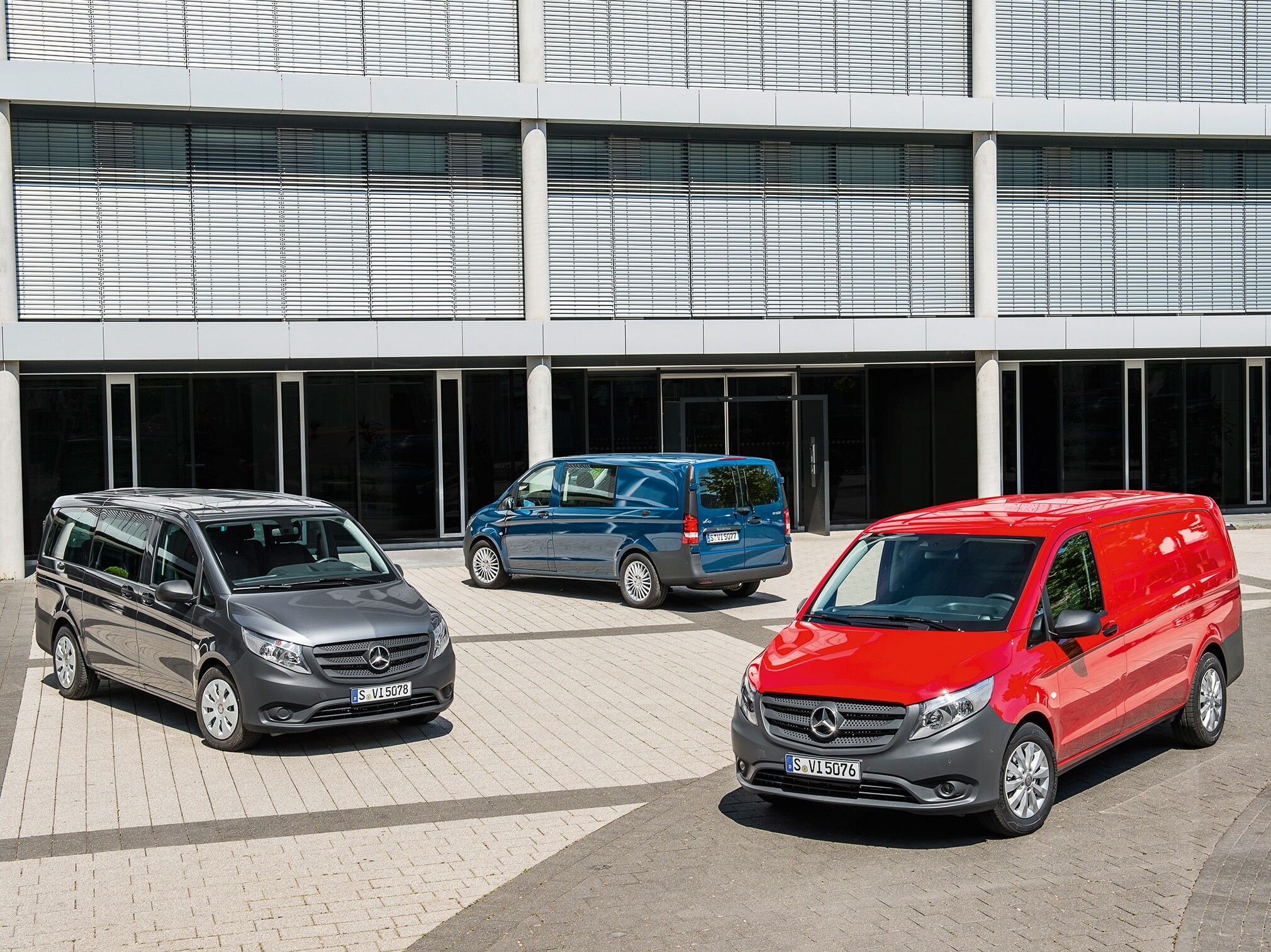 Several Mercedes-Benz Vitos parked in front of modern office building