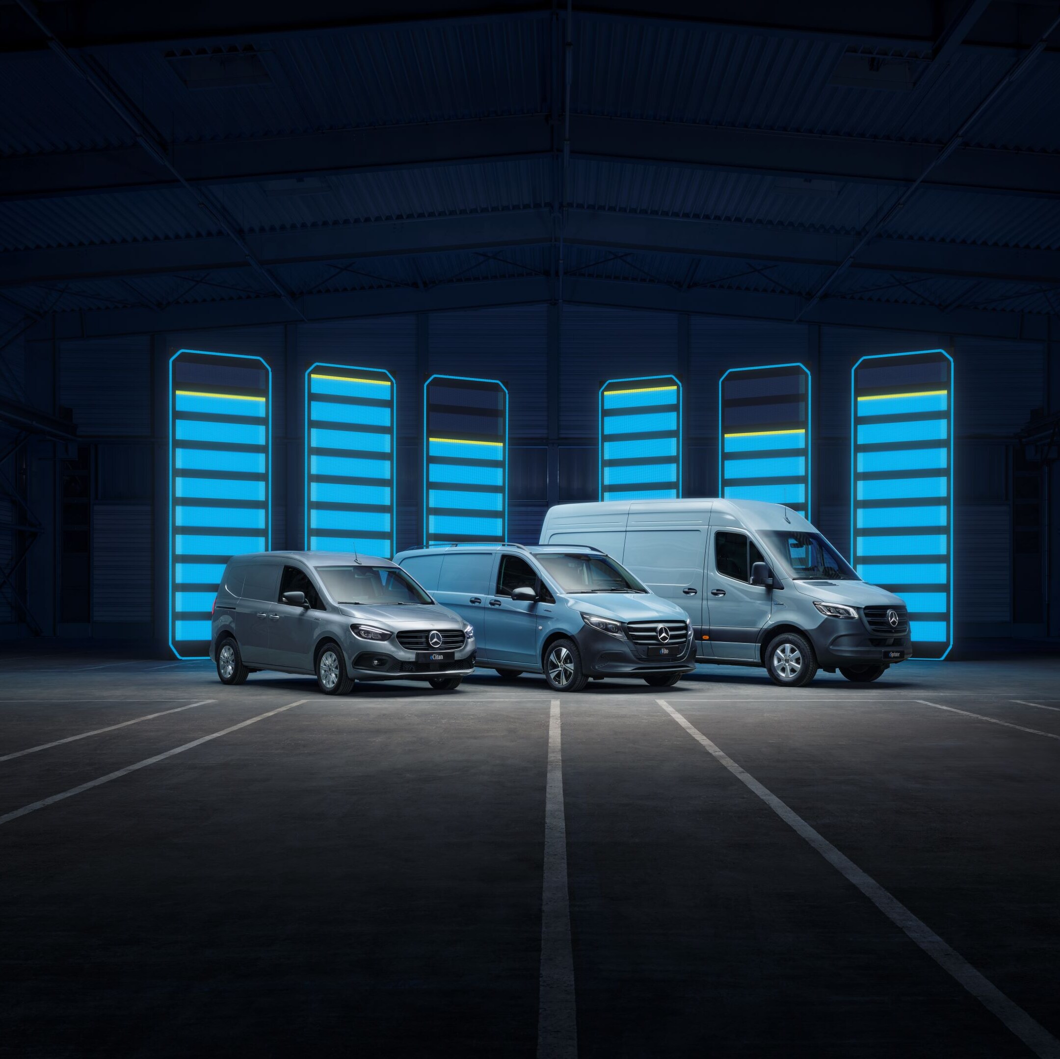 Three Mercedes-Benz panel vans – a grey Sprinter, a blue Vito, and a yellow Citan – positioned on a rooftop with a cityscape backdrop.