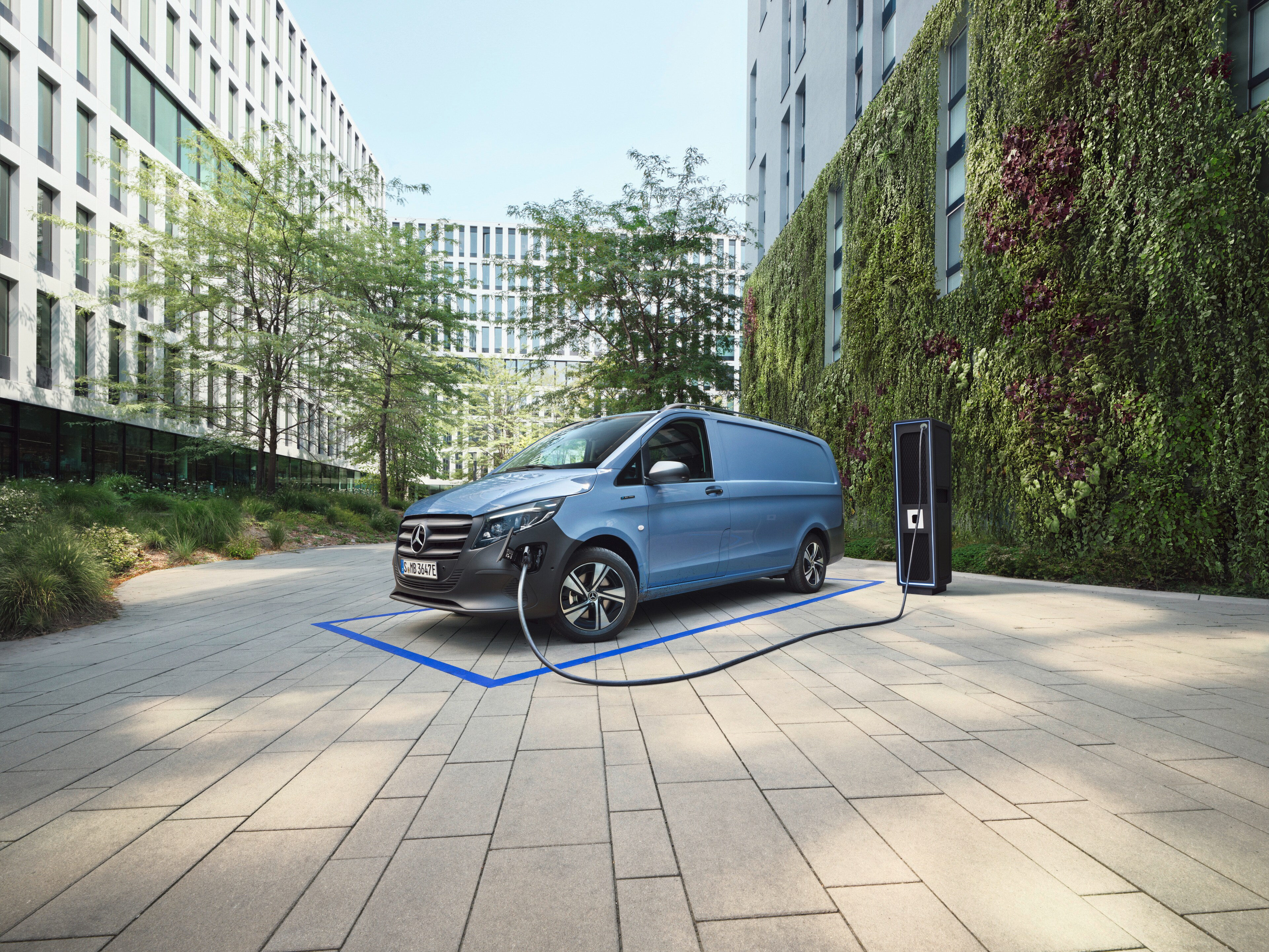 Light blue Mercedes-Benz eVito Panel Van plugged into a charger outside an office building.