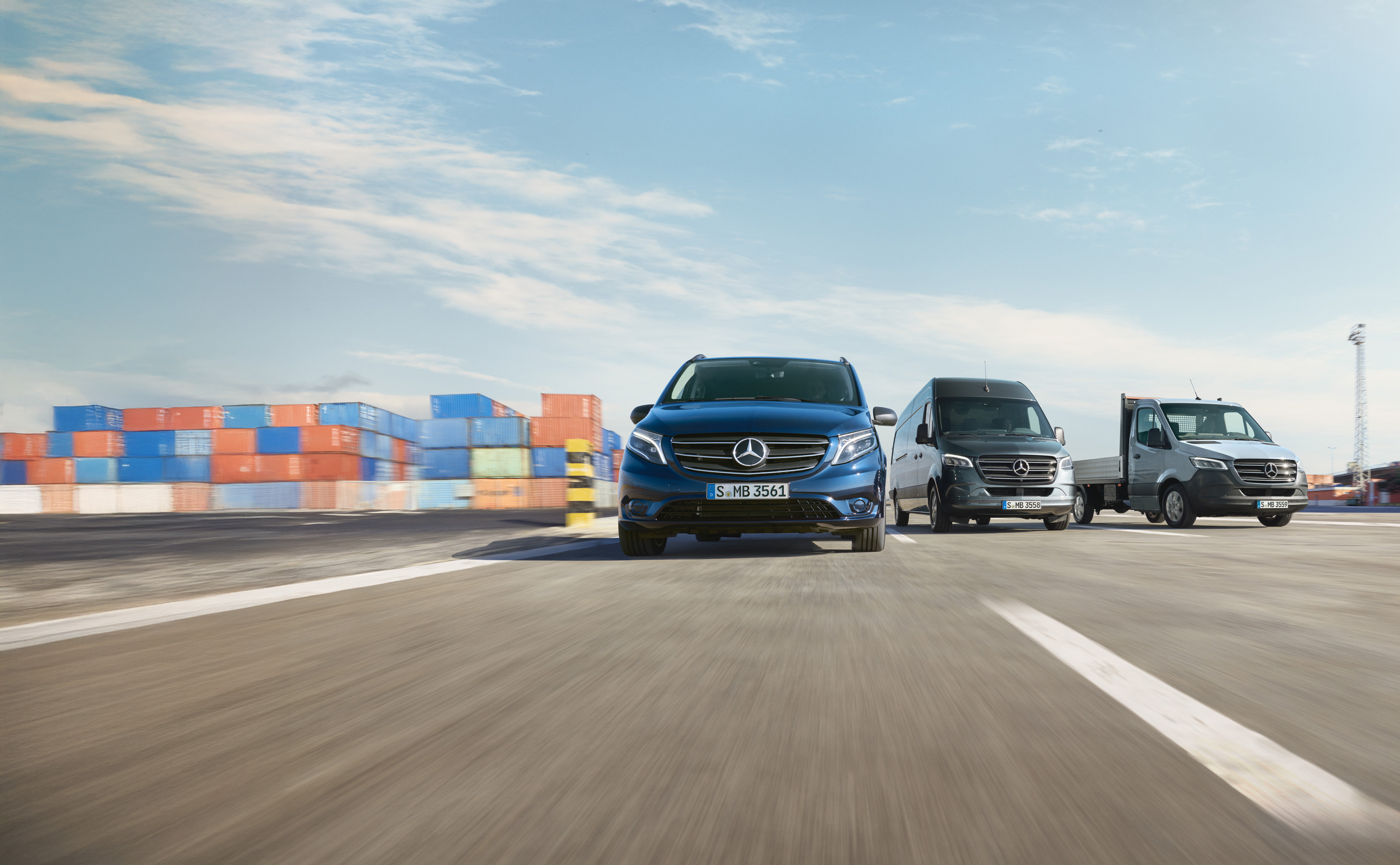 Mercedes-Benz | Vans Care | Service24h A range of Mercedes-Benz vans parked side-by-side on a road next to a shipping dock.