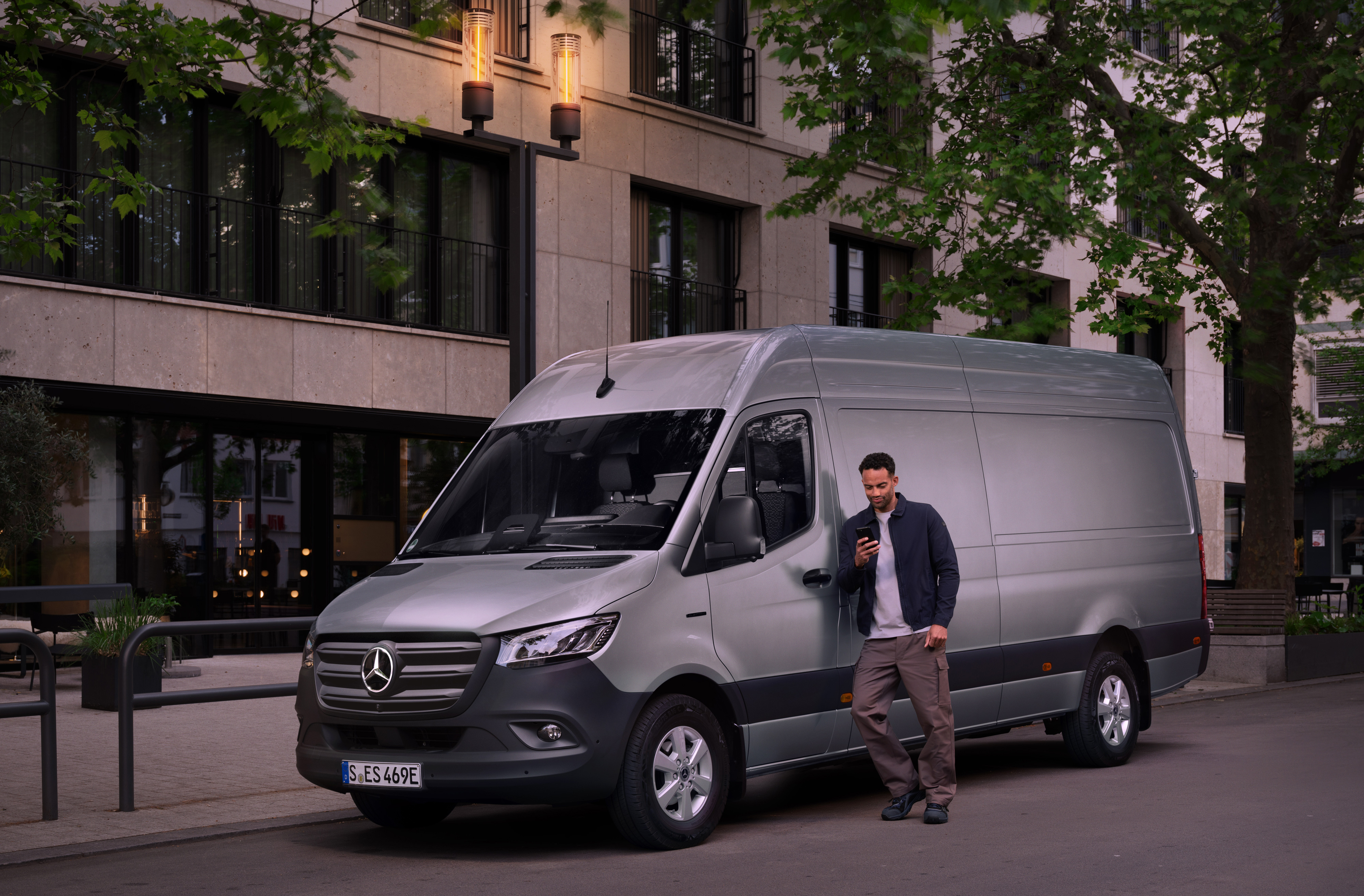Mercedes-Benz | Van care | Customer Assistance Center Man leaning on a silver Mercedes-Benz Sprinter van and using his smartphone – speedy assistance from Mercedes Benz Customer Care.