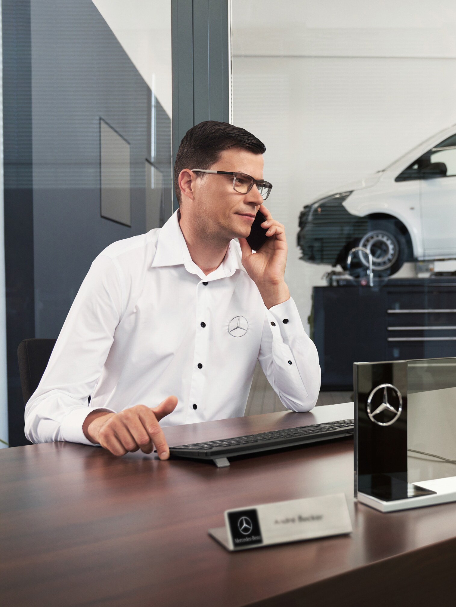 Mercedes-Benze employee talks on the phone at a desk with a Mercedes-Benz Vito van in the workshop.