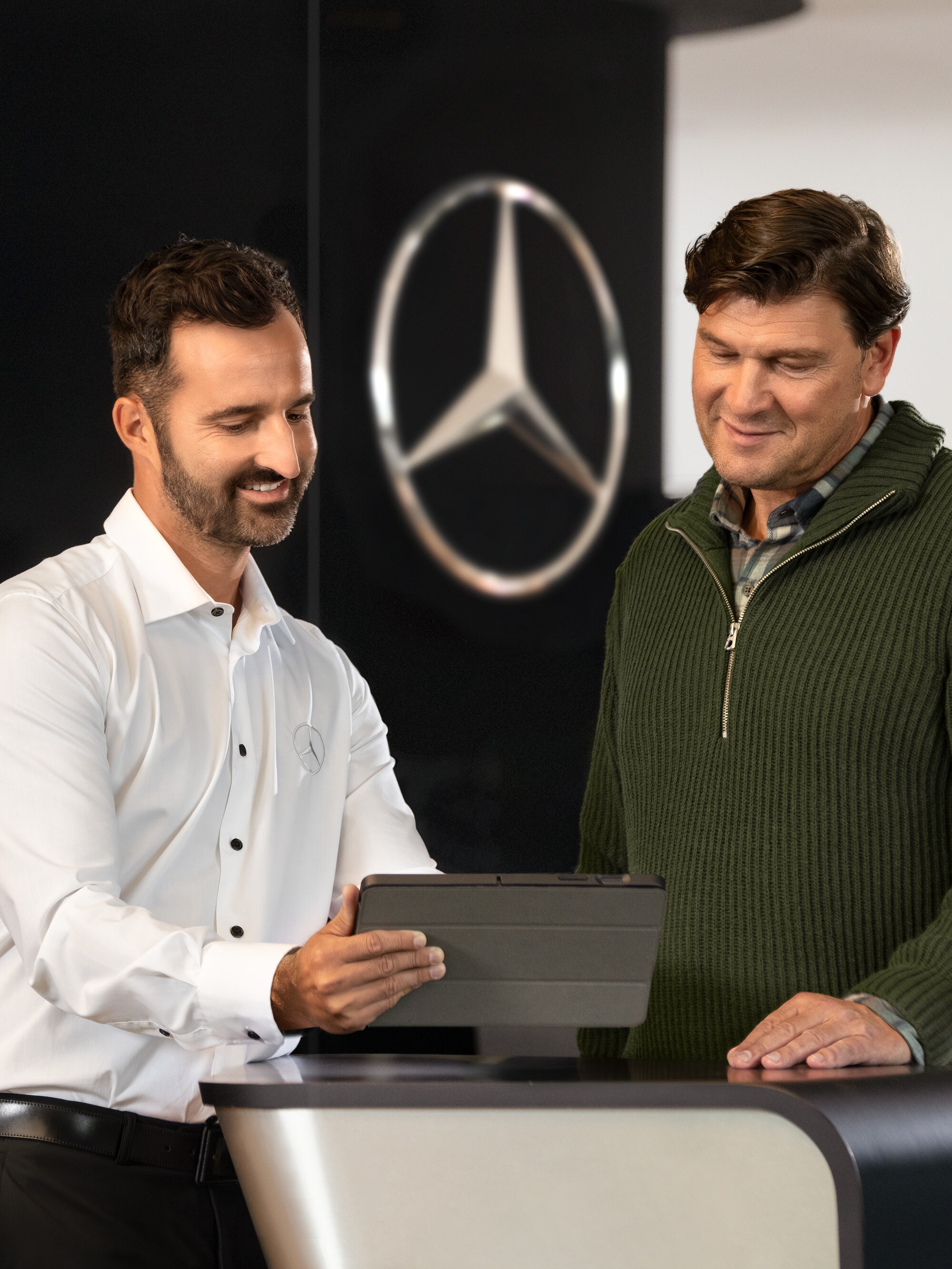 Mercedes employee advises customers at the counter with a tablet – individual support and commercial advice in the dealership.