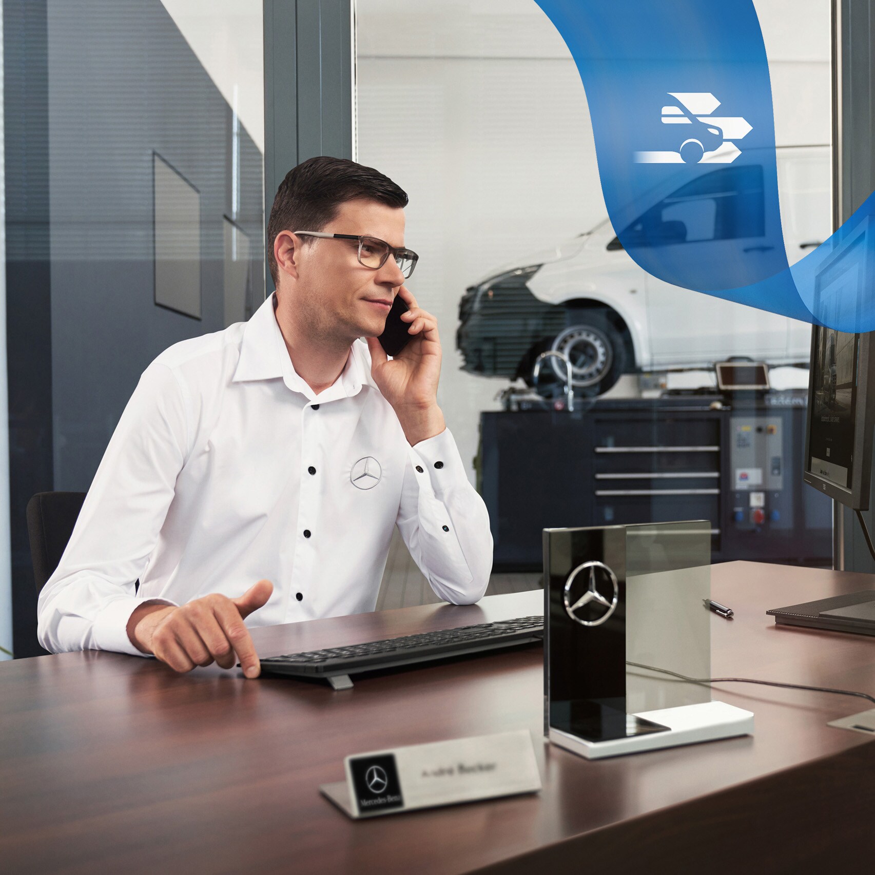 An employee at a desk on the phone and a Mercedes-Benz Vito van in the workshop in the background.