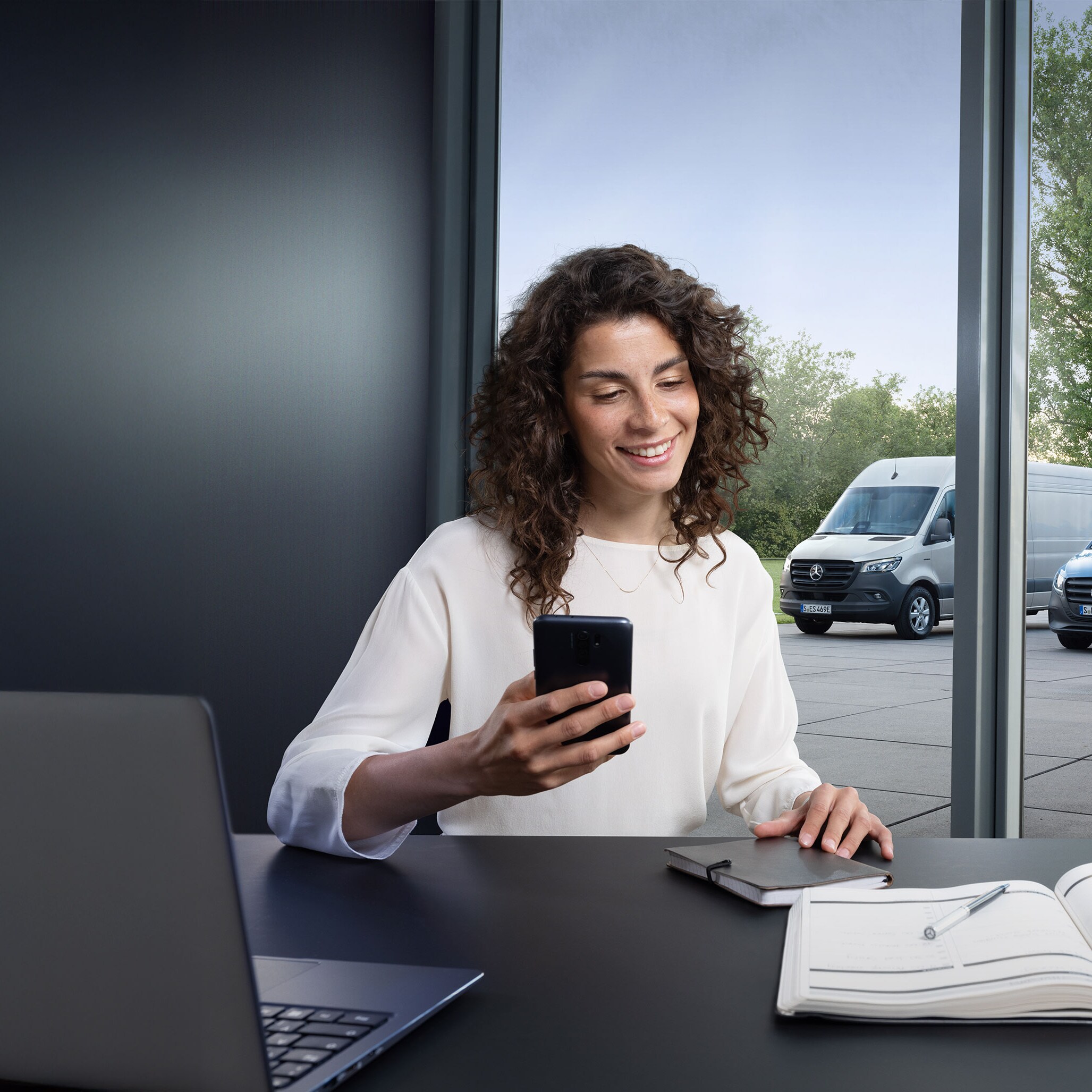 Woman looking for a Mercedes-Benz Authorised Repairer on her smartphone with a range of Mercedes-Benz vans in the background.