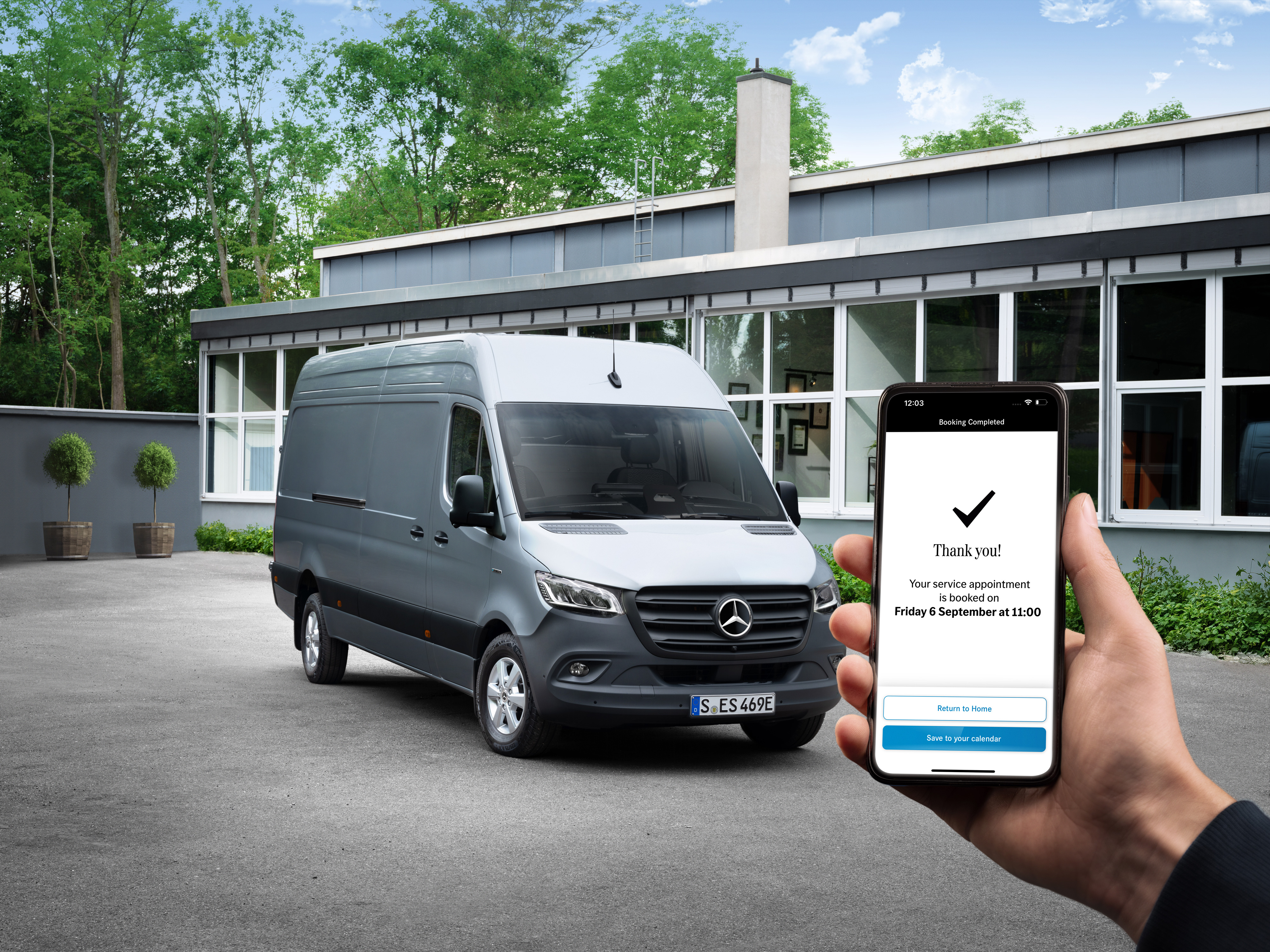 Mercedes-Benz | Convenience | Authorised Repairer A grey Mercedes-Benz Sprinter van in front of a office with a person holding a smartphone in the foreground.