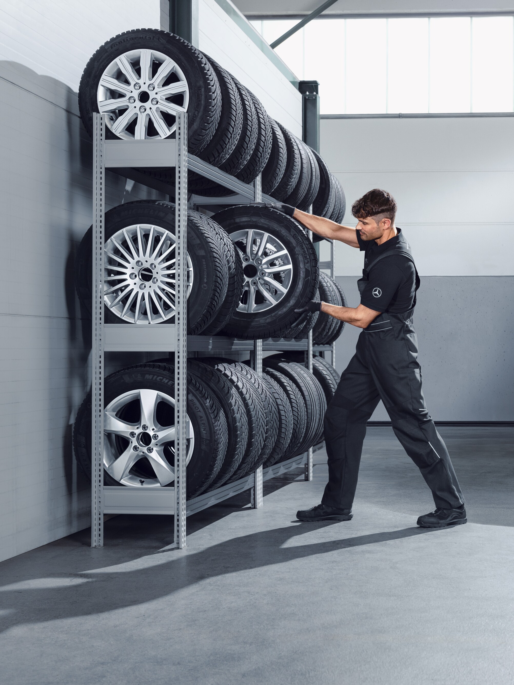 Mechanic selecting Mercedes-Benz complete winter wheels for a white Sprinter from the workshop shelf.