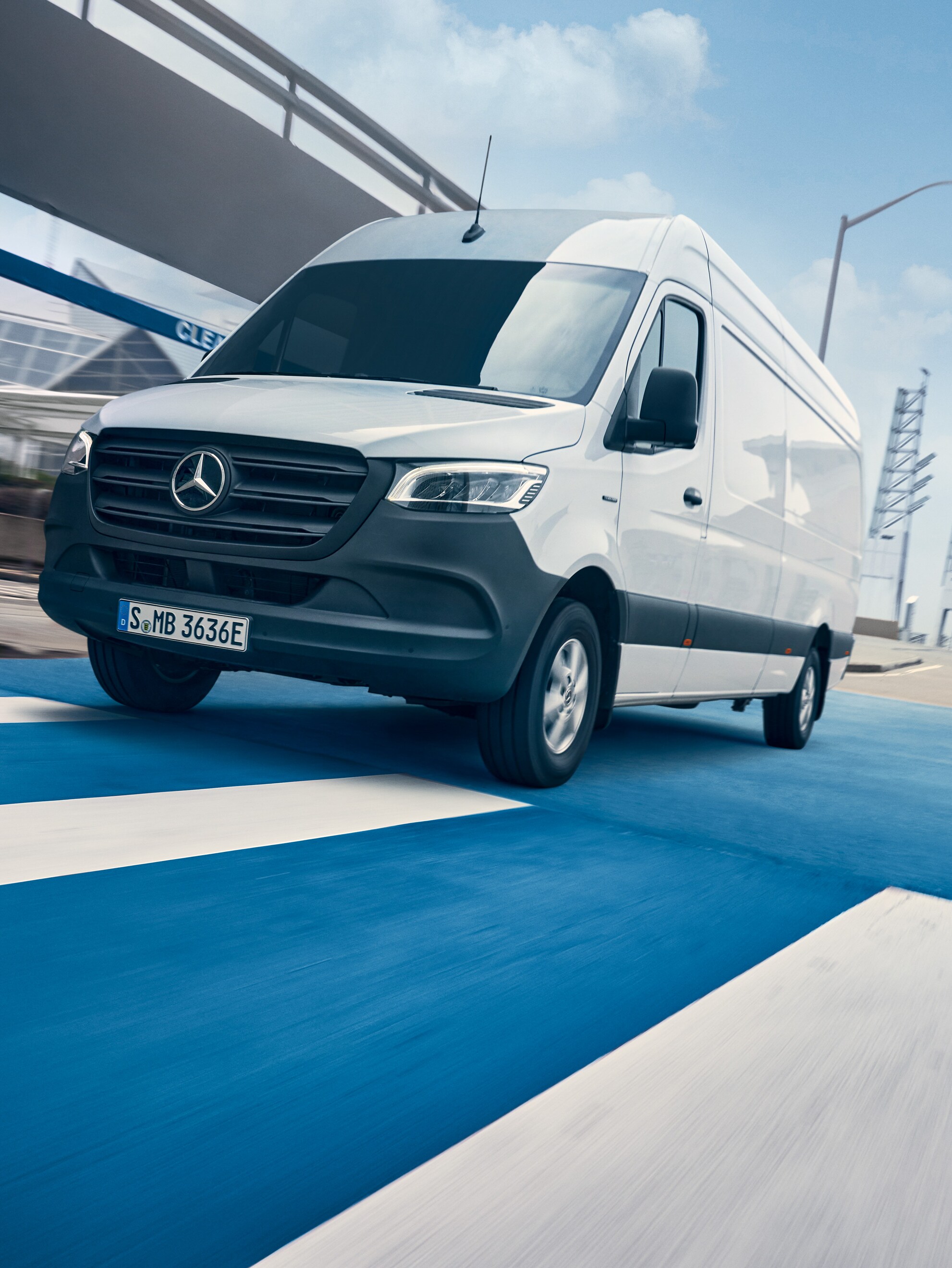 A white Mercedes-Benz Sprinter drives on a road through a city.