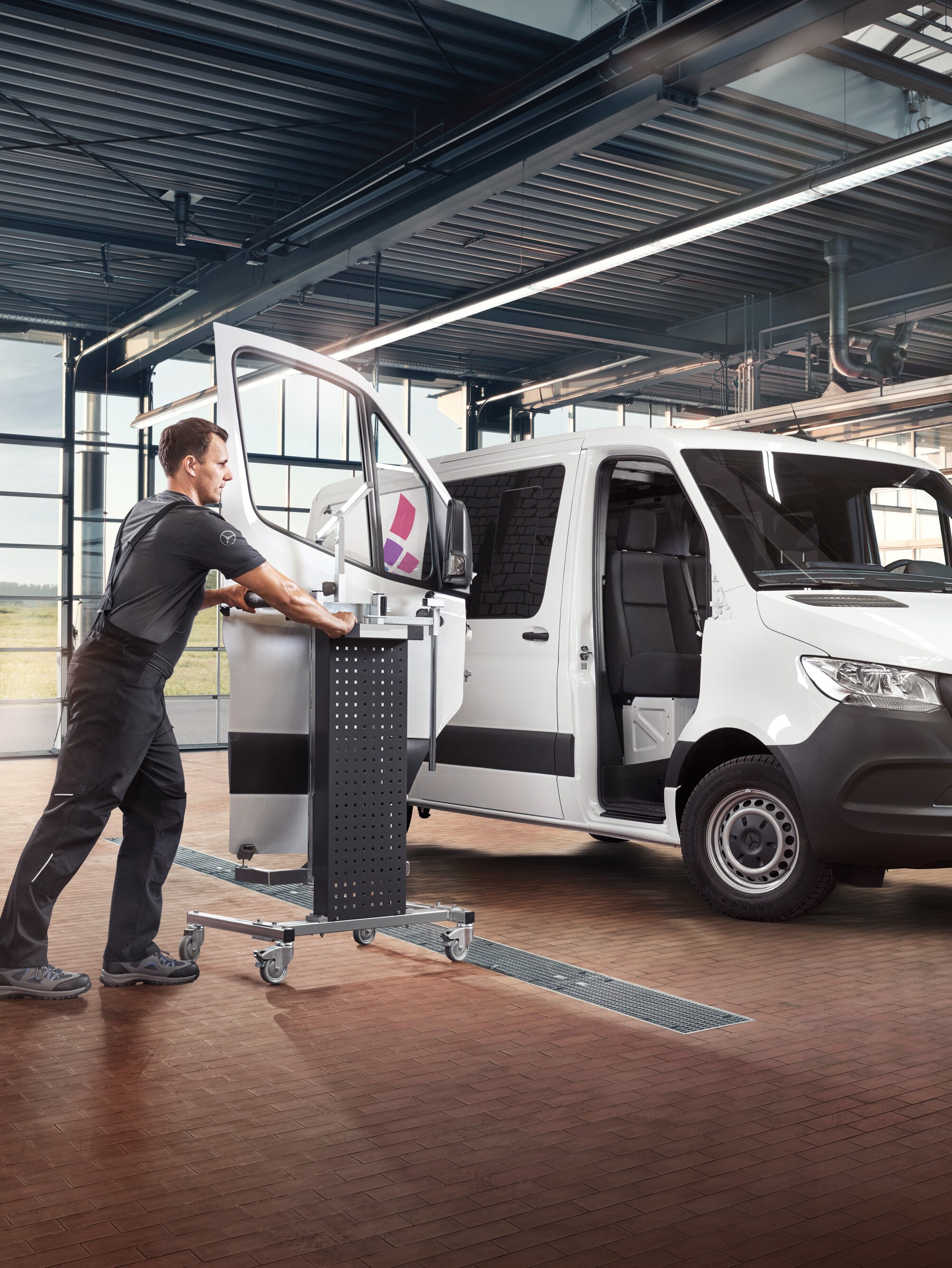 A technician maintains the passegner door of a white Mercedes-Benz Sprinter van.