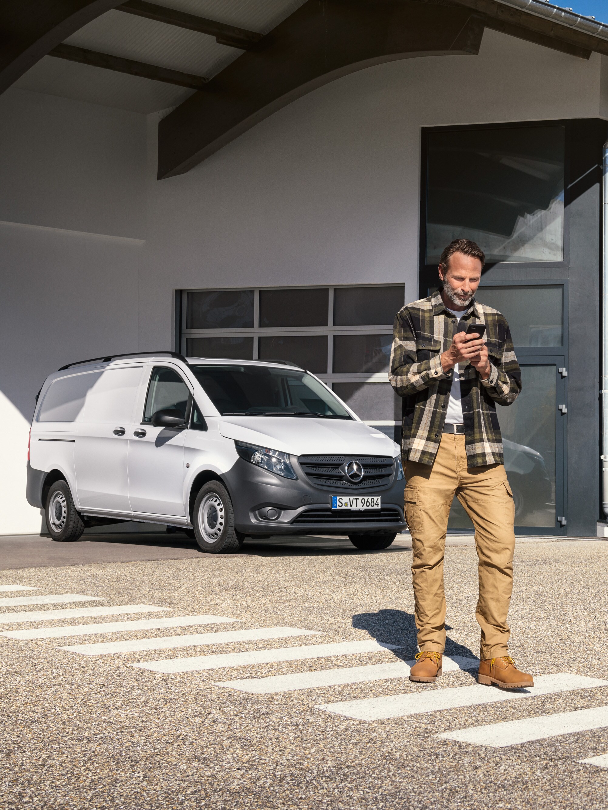 A man standing in front of a white Mercedes-Benz Vito van using his smartphone.