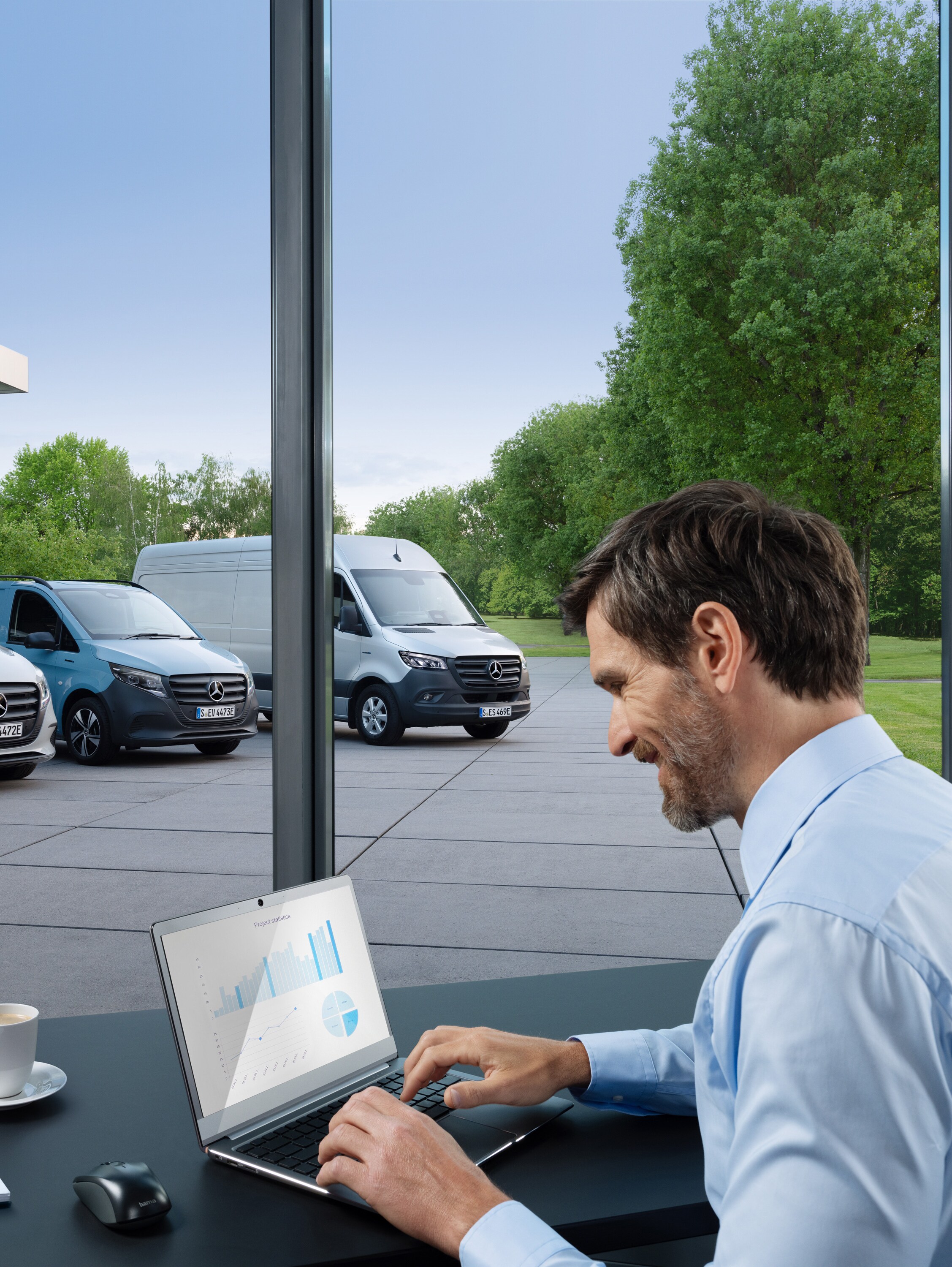 A man working on a laptop, outside there is a range of Mercedes-Benz vans.