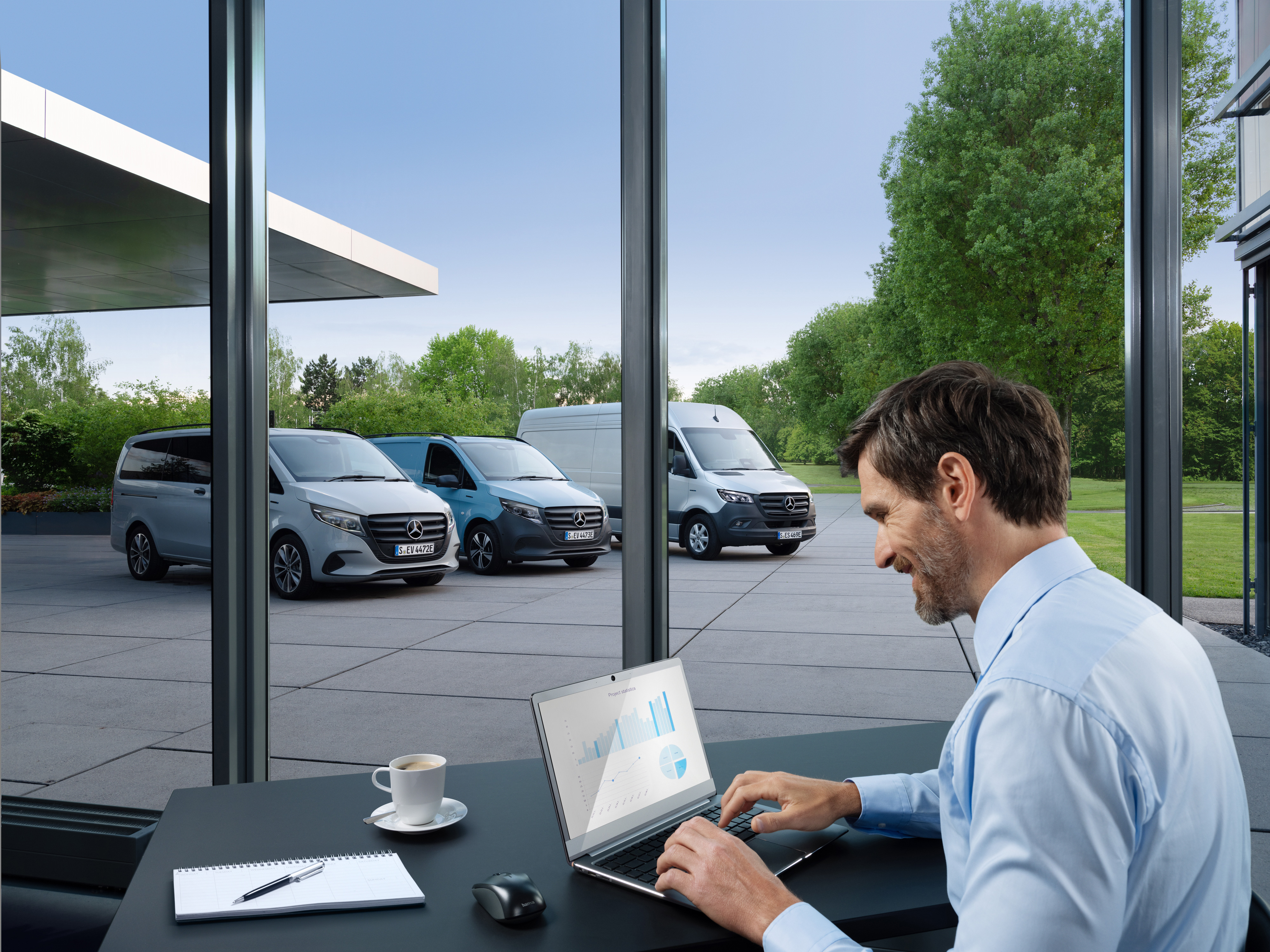 Mercedes-Benz | Electric Vehicle Service | Packages A man working on a laptop, outside there is a range of Mercedes-Benz vans.