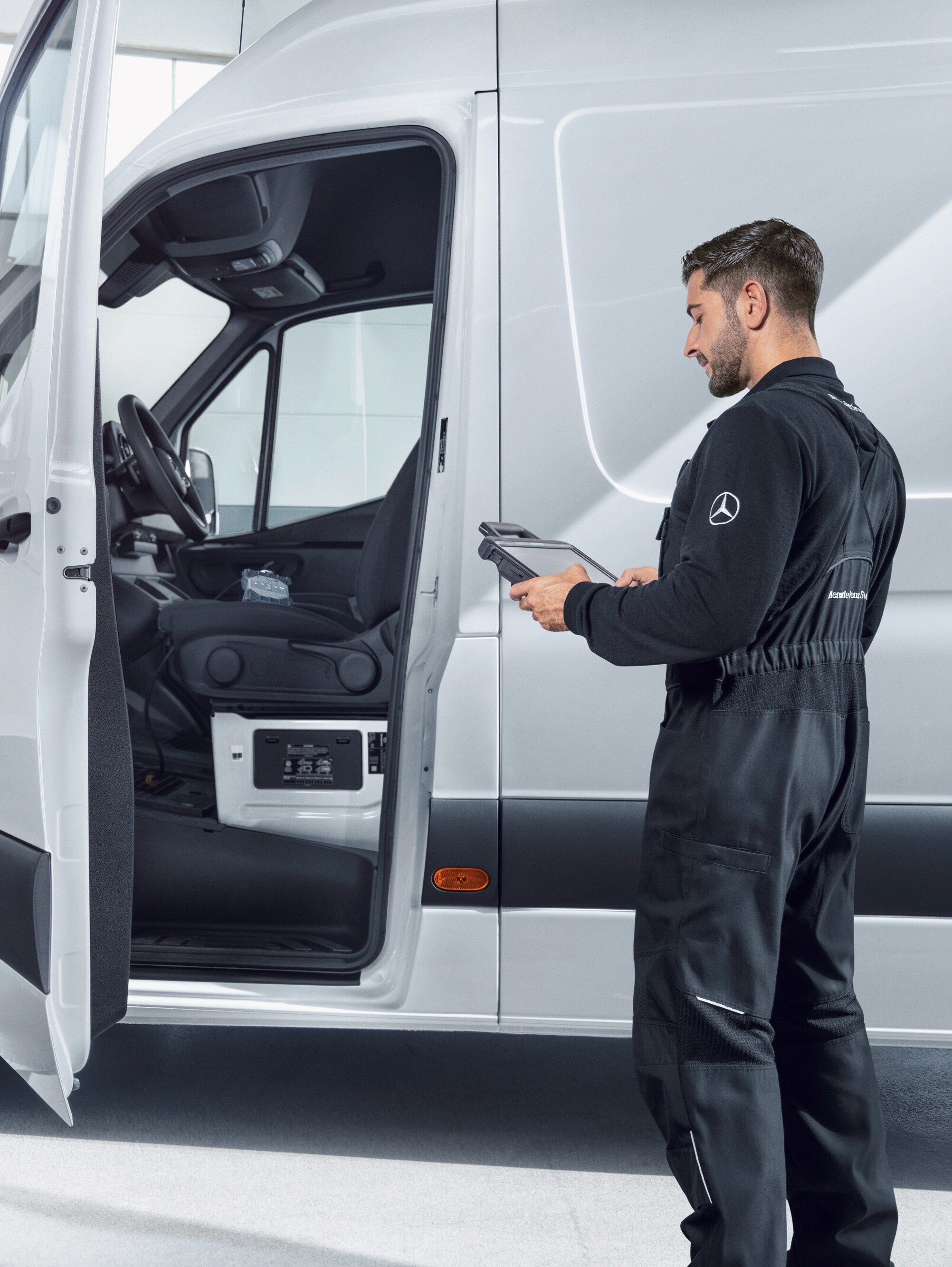 A technician checks a white Mercedes-Benz Sprinter van with a tablet.