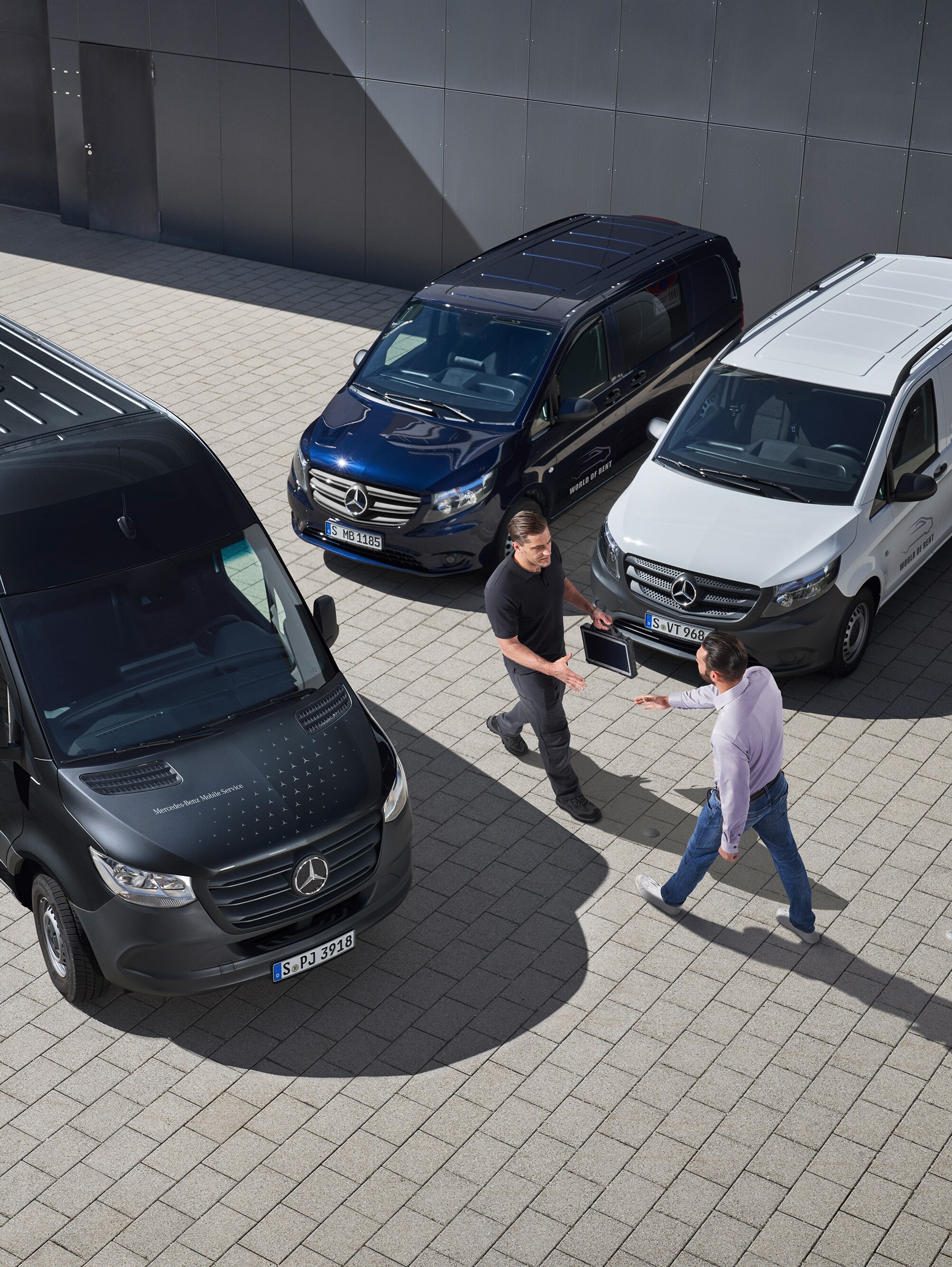 A Mercedes-Benz technical liaison officer greets a customer in a carpark walking in between three Mercedes-Benz vans.
