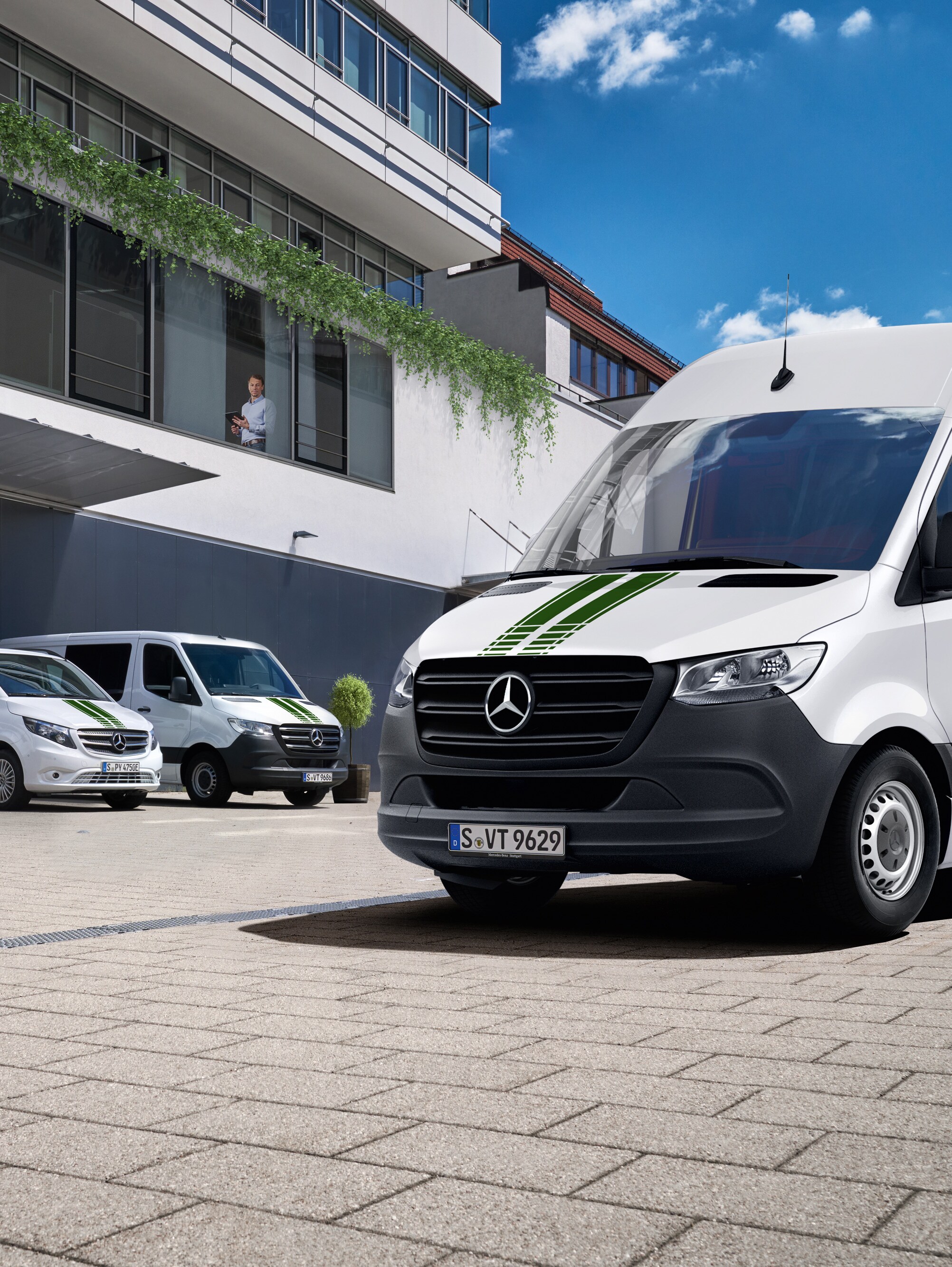 A fleet of white Mercedes-Benz vans in front of an office building on a sunny day with blue skies.