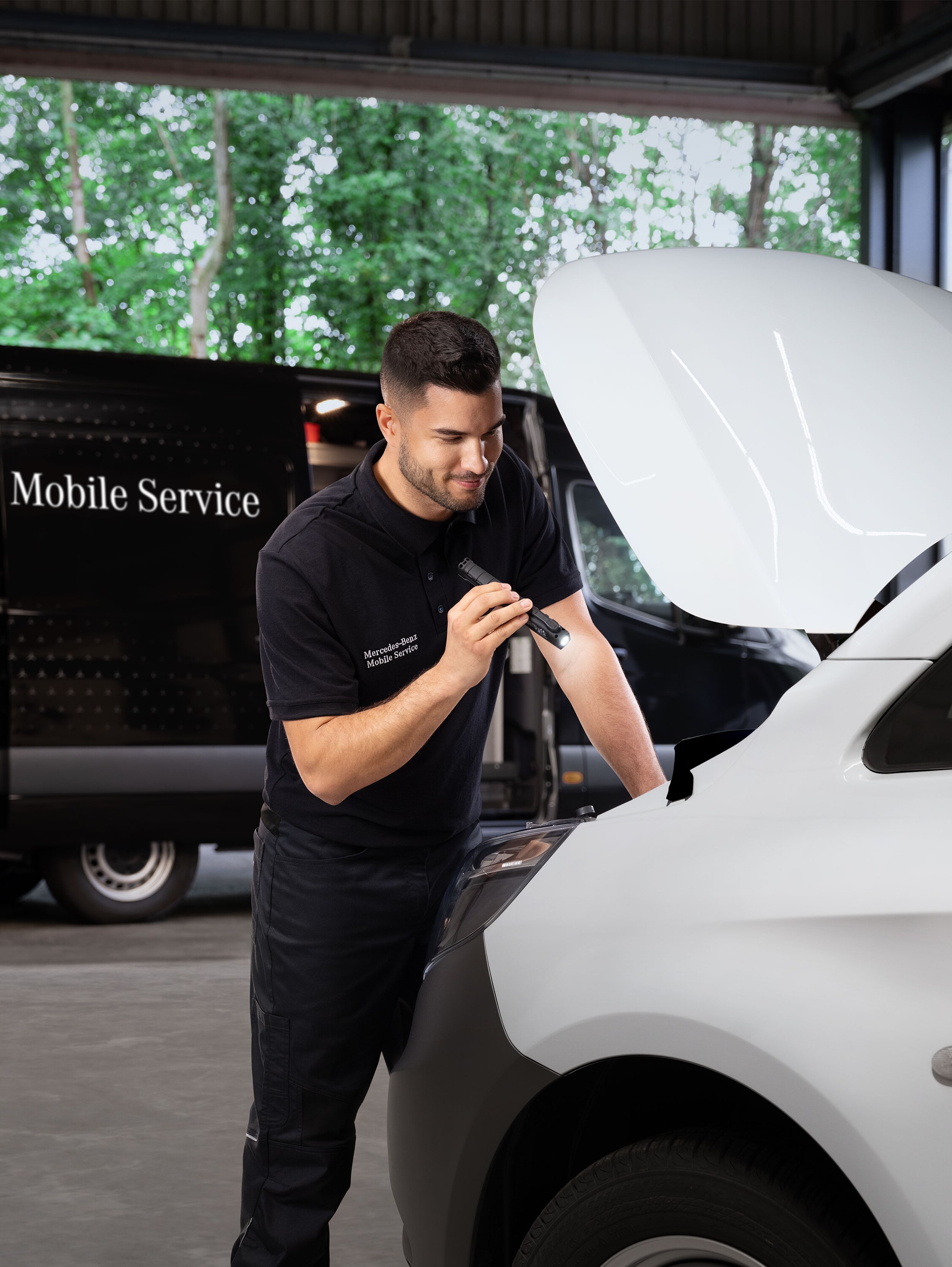 Mechanic inspecting the engine of a white Mercedes-Benz van.