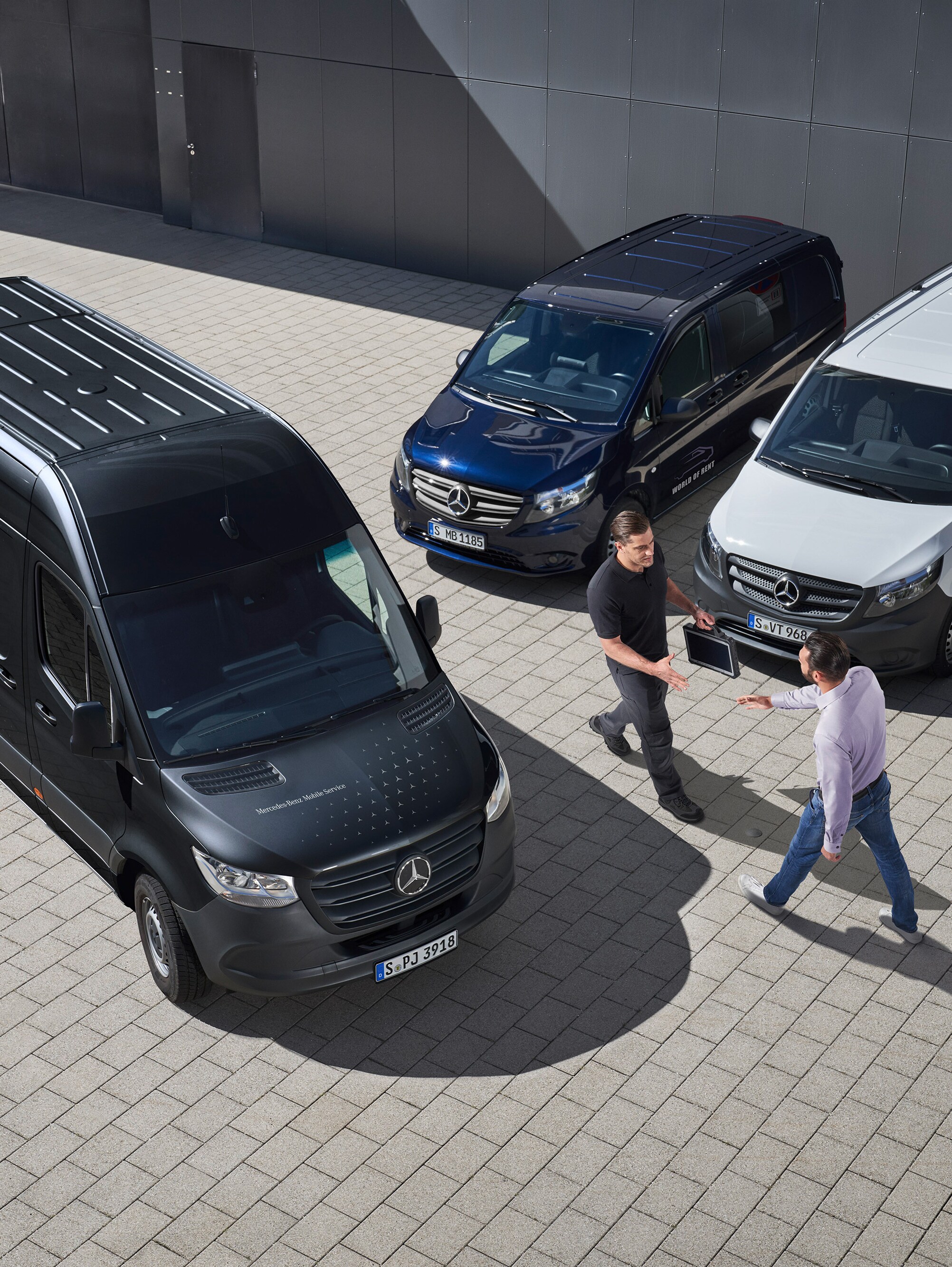 Two men greet each other amongst Mercedes-Benz vans.