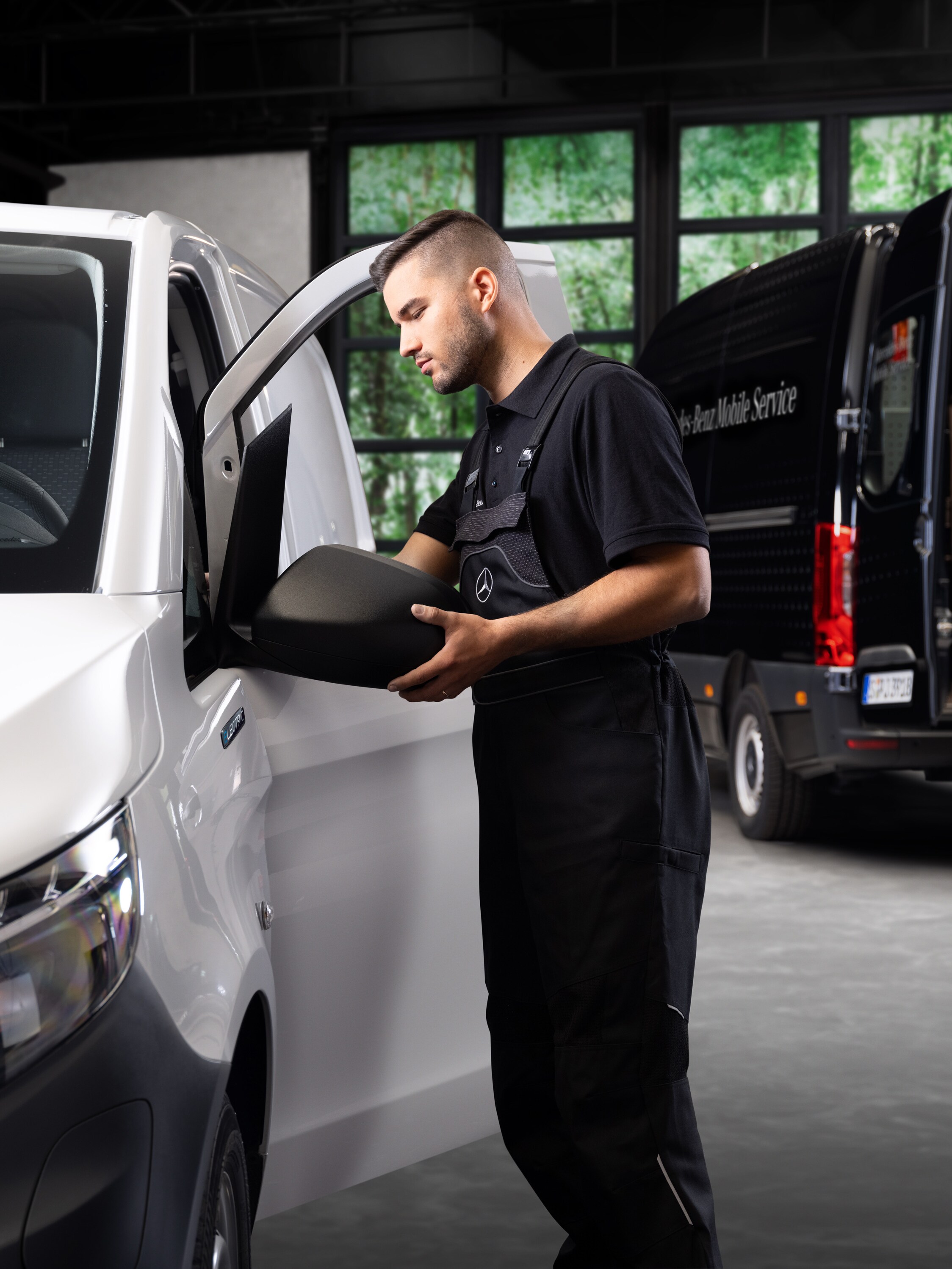 A technician replaces an exterior mirror on a white Mercedes-Benz Vito van.