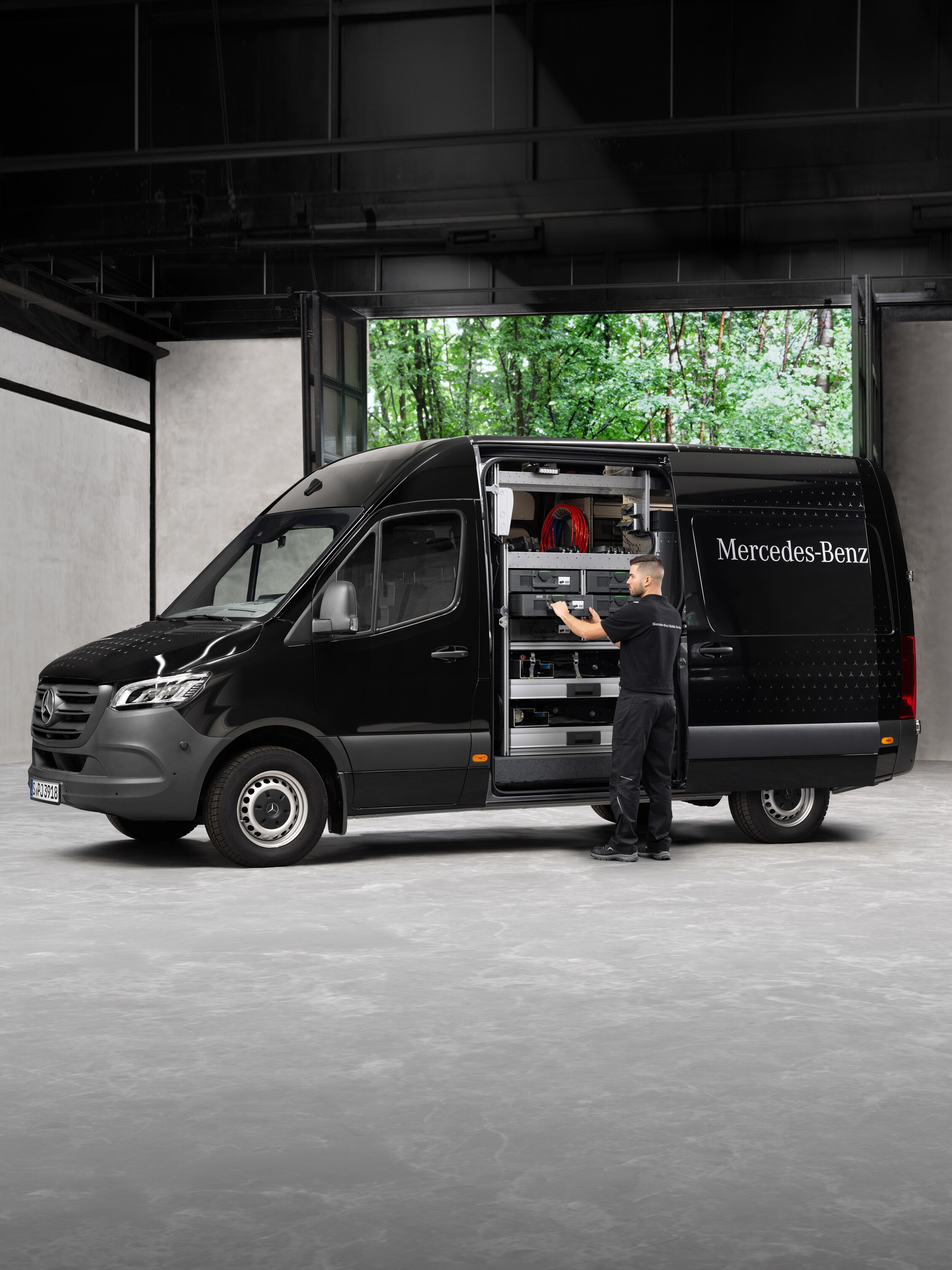 A technician removes tools from a black Mercedes-Benz Sprinter van.