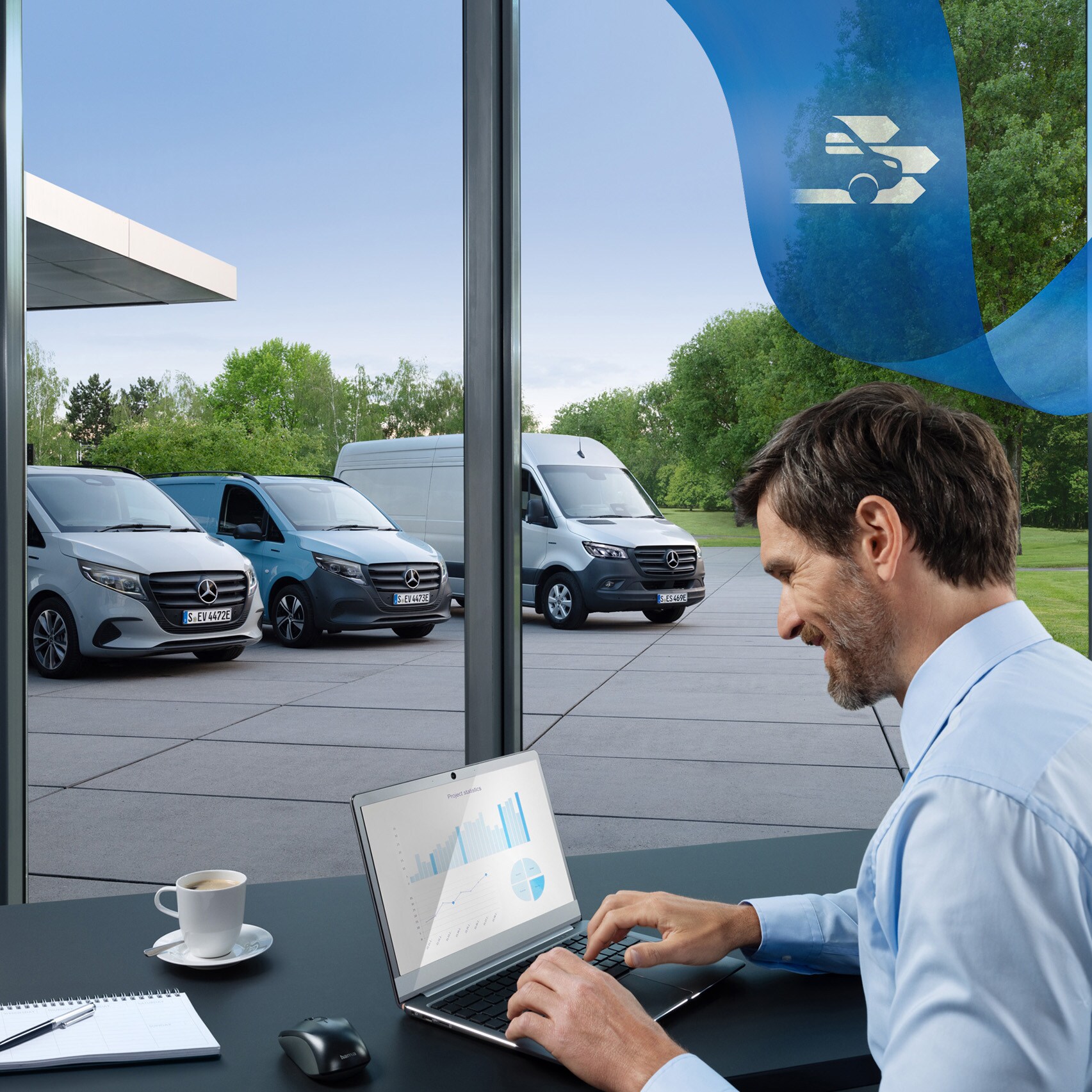 A man is using a laptop in an office with a range of Mercedes-Benz vans in the background.