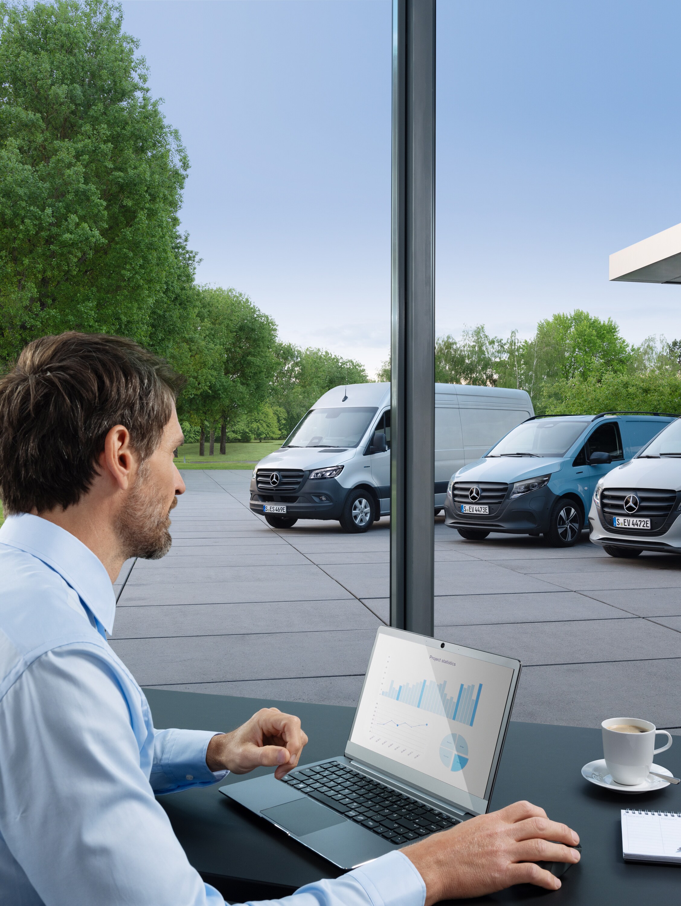 Man monitoring several parked Mercedes-Benz vans with a laptop, symbol of digital fleet management.