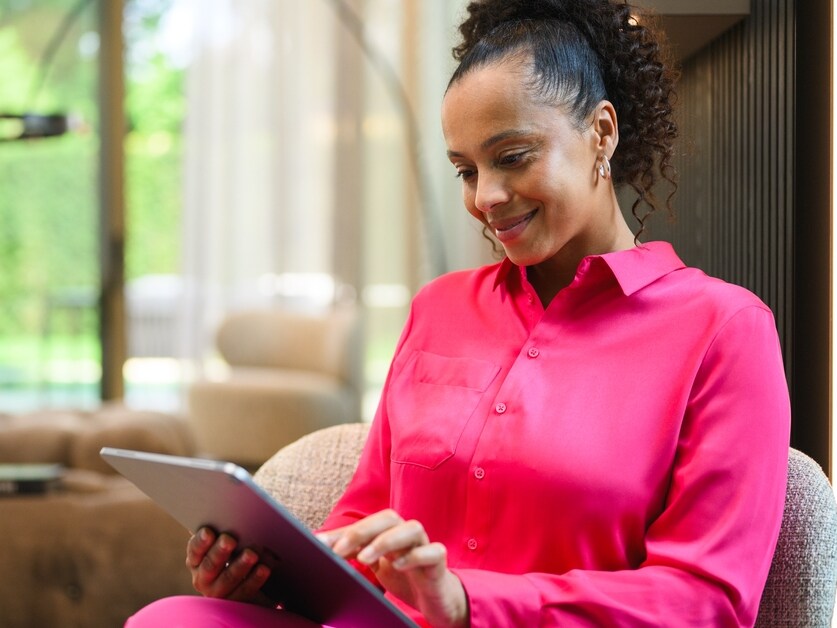 A person at home looking at a tablet device and smiling.