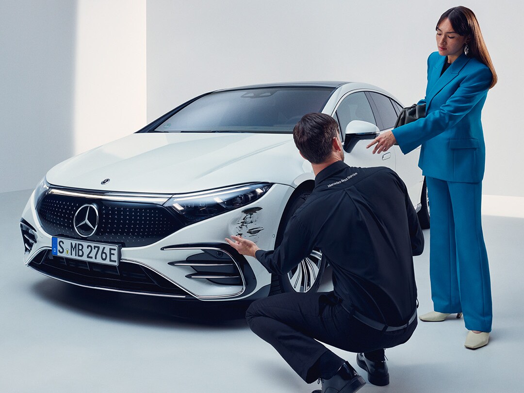 Customer and vehicle specialist inspecting damage on a white Mercedes-Benz car.