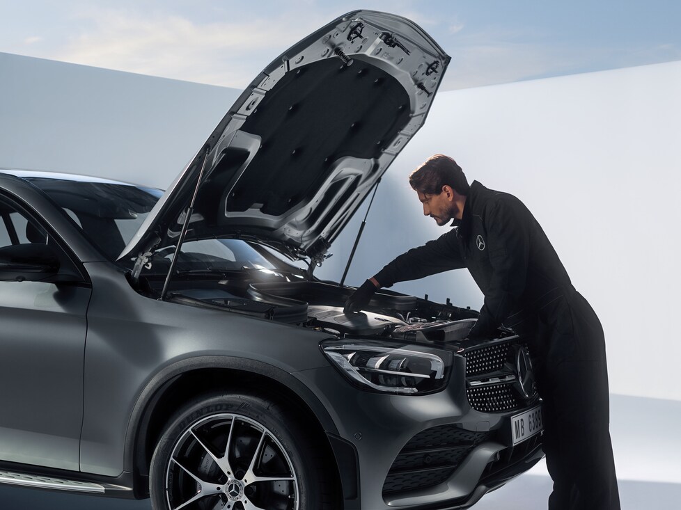 Technician inspecting the engine of a Mercedes-Benz car with the bonnet open.