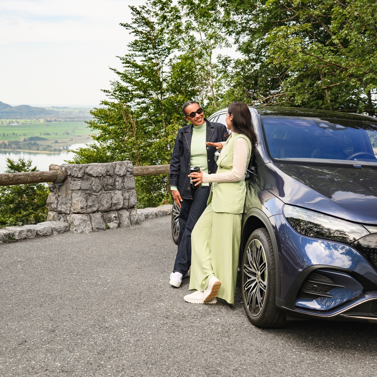 Two people stood next to their Mercedes-Benz near a lake.