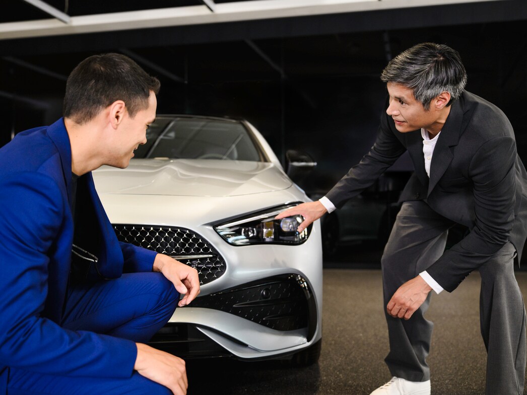 Two people inspecting the front of a Mercedes-Benz car in a showroom  