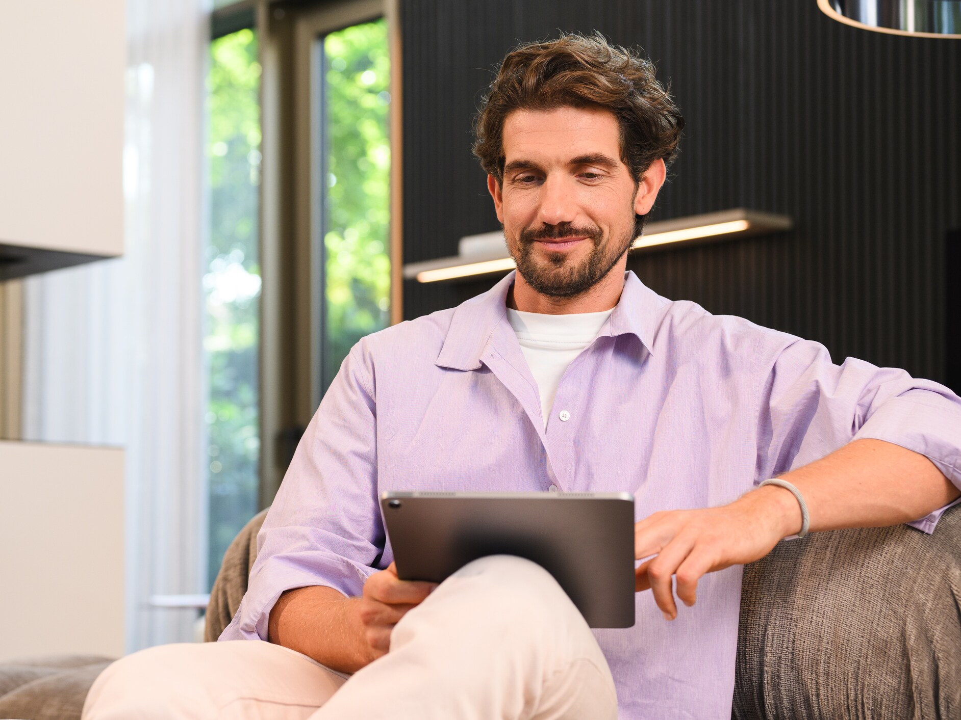 Man in lilac on a sofa using a tablet.