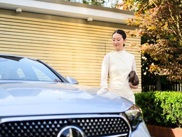 A person standing next to a Mercedes-Benz outside their house.
