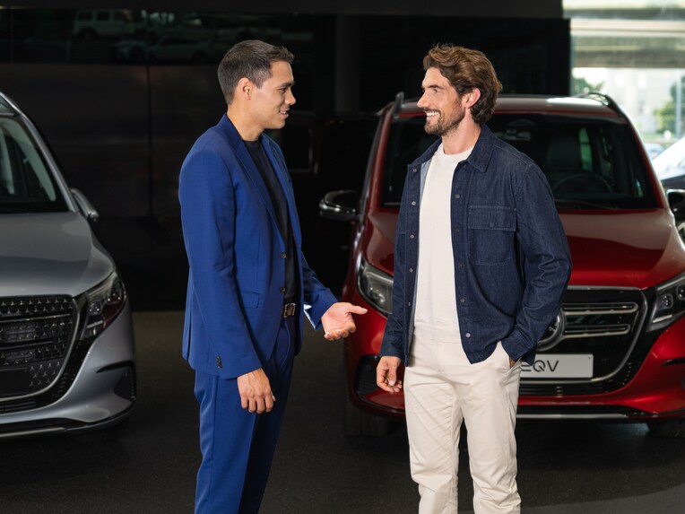 Two people talking to each other in front of two Mecedes-Benz vans.