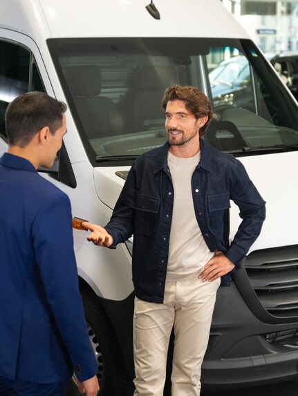 Two people talking to each other in front of a Mercedes-Benz Sprinter Panel Van.
