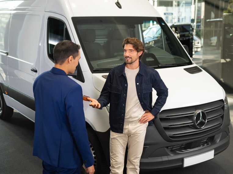 Two people talking to each other in front of a Mercedes-Benz van.